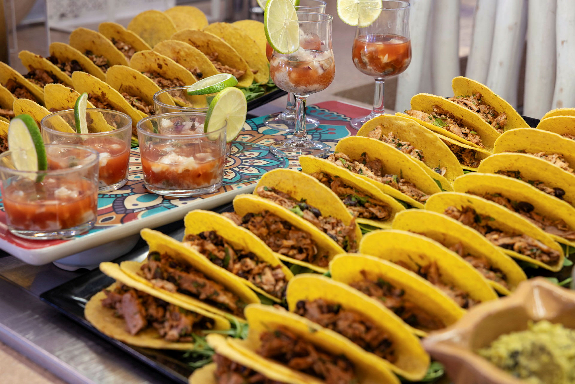Bild på flera tacos fyllda med kött och grönsaker, servade på brickor tillsammans med glas med dryck och limeklyftor. (AI-genererad text)