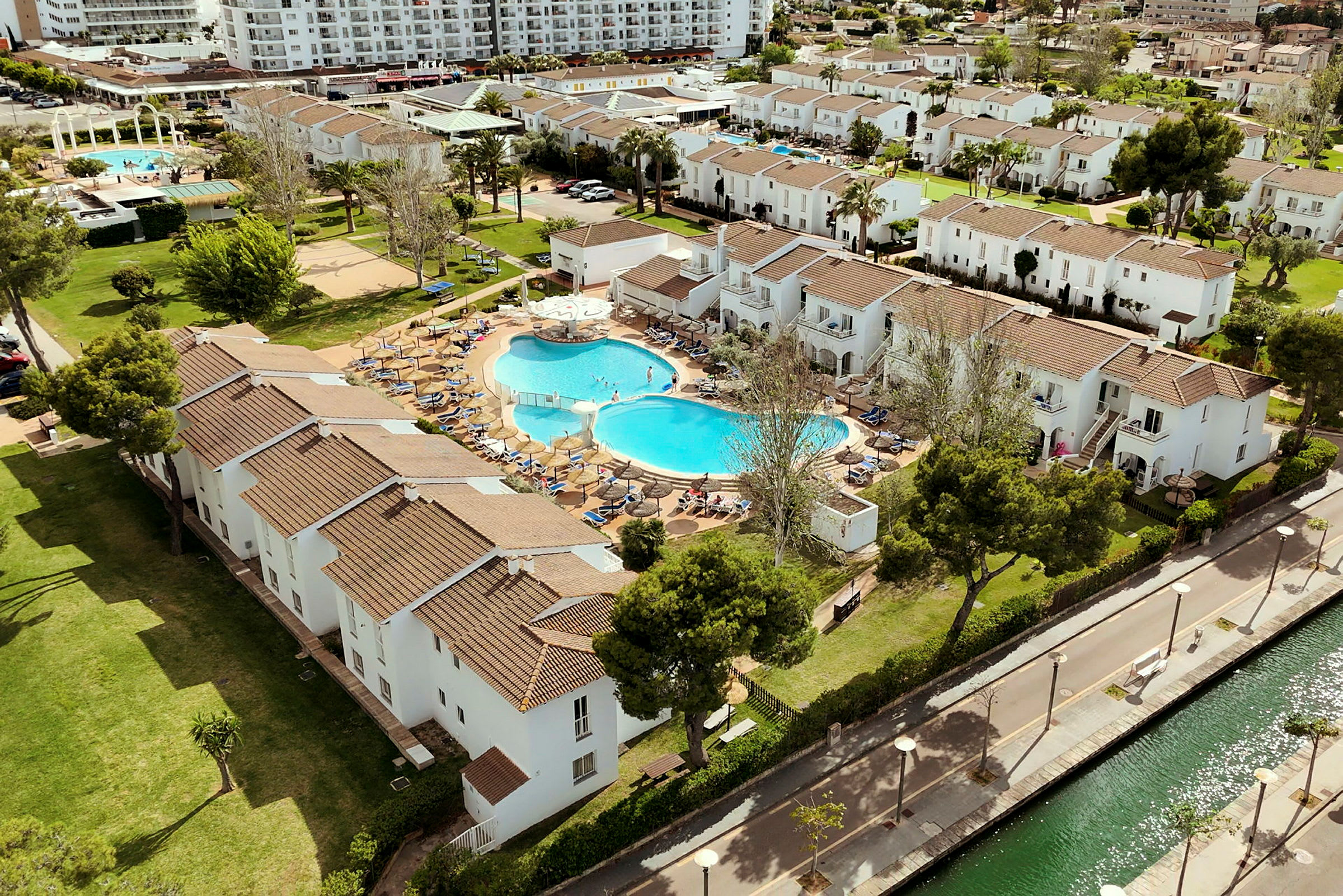 En flygbild av ett semesterkomplex med vita byggnader, en pool och grönområden. (AI-genererad text)
