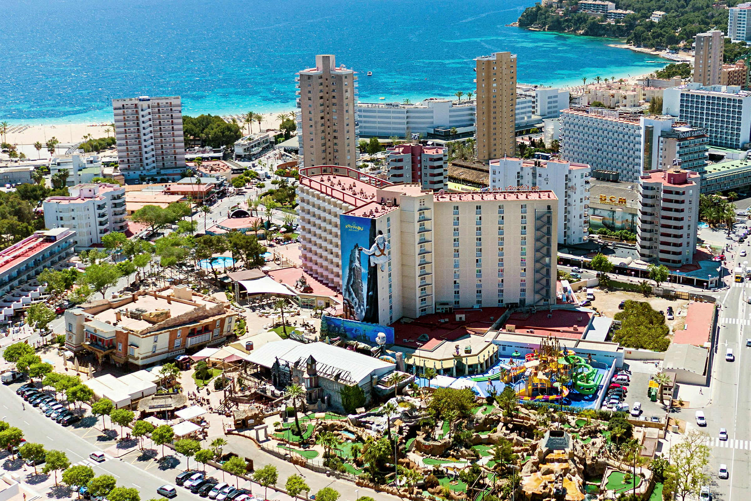 Flygfoto av en kuststad med hotellbyggnader, strand och ett nöjesområde. (AI-genererad text)