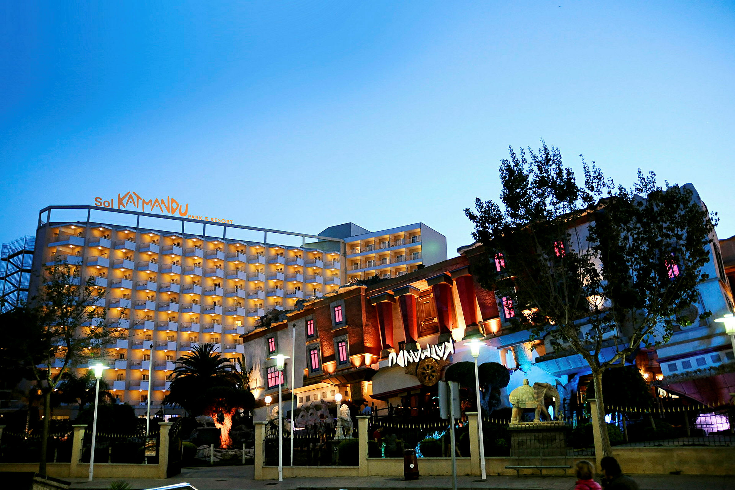 Ett hotell med namnet Sol Katmandu Park & Resort, belyst på kvällen, omgivet av en trädgård. (AI-genererad text)