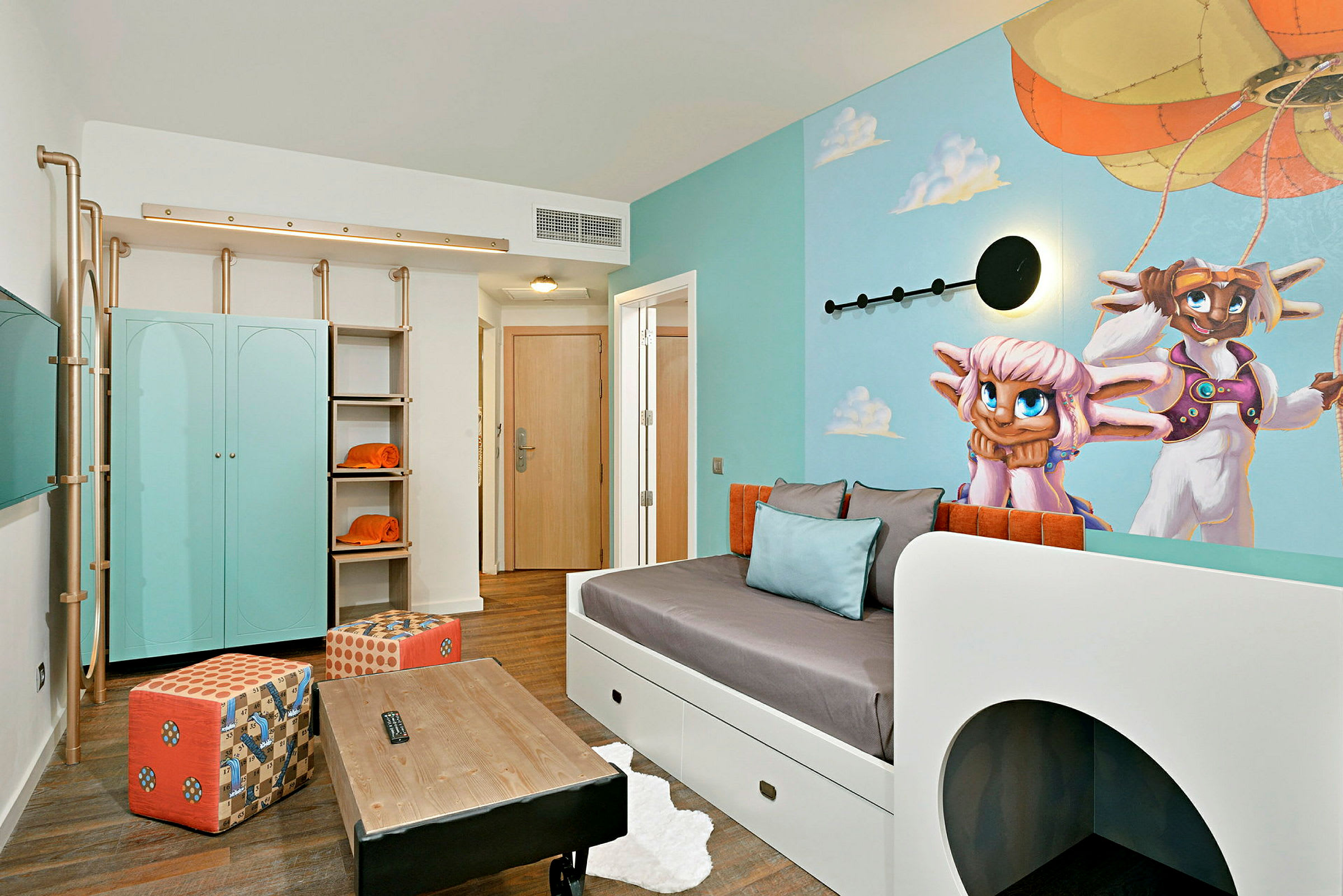 Ett hotellrum med en ljus och färgglad inredning, inklusive ett blått skåp, orange detaljer och en väggmålning av två karaktärer framför en luftballong. (AI-genererad text)