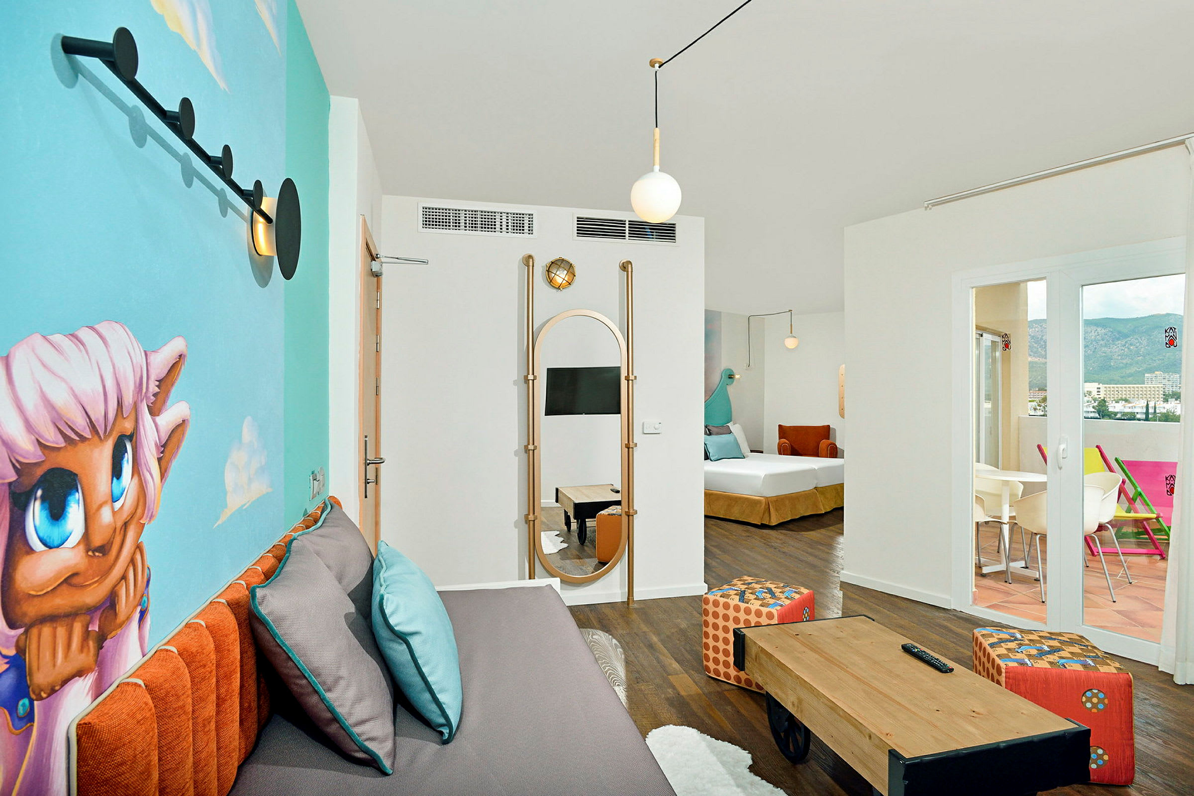 Ett modernt och färgglatt hotellrum med en väggmålning, en soffa med kuddar, ett litet bord, och en terrass med utsikt. (AI-genererad text)