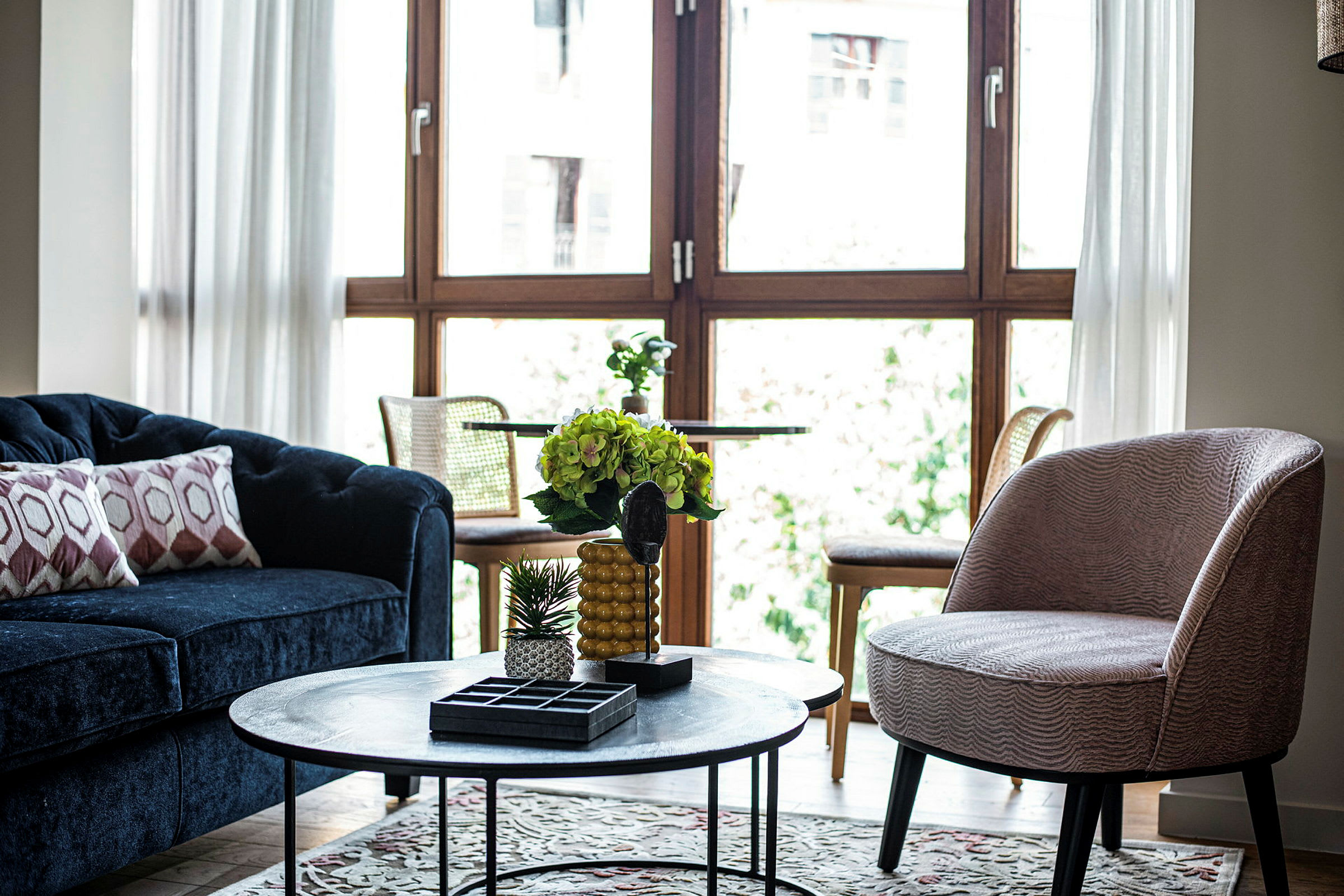 Vardagsrum med blå soffa, rund bordslampa och stora fönster. (AI-genererad text)