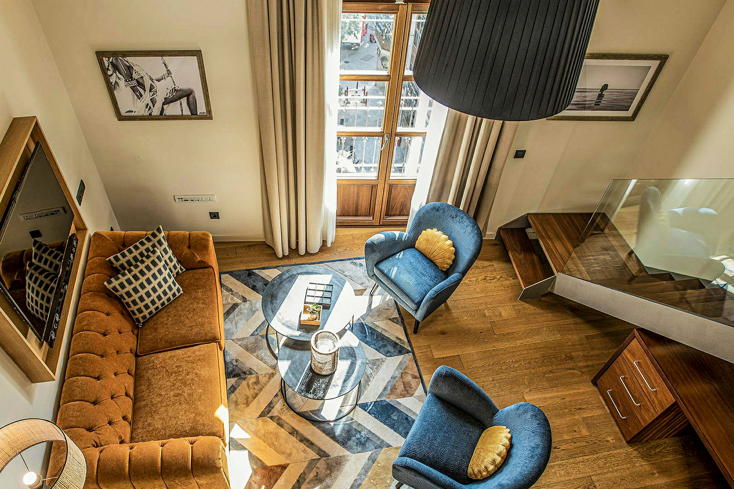 Ett vardagsrum med en brun soffa, två blå stolar, ett glasbord, och trädetaljer. Tavlor hänger på väggarna. (AI-genererad text)