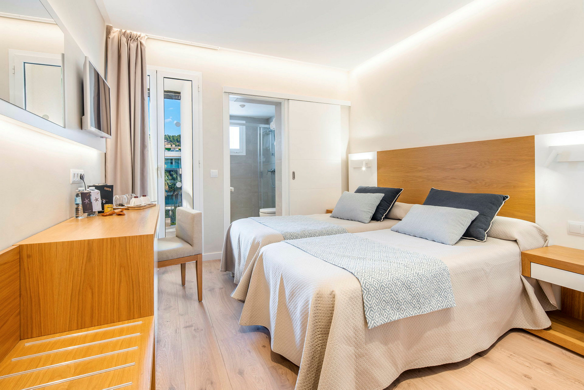 Ett hotellrum med två enkelsängar med trädetaljer, en arbetsyta och avskilt badrum. (AI-genererad text)