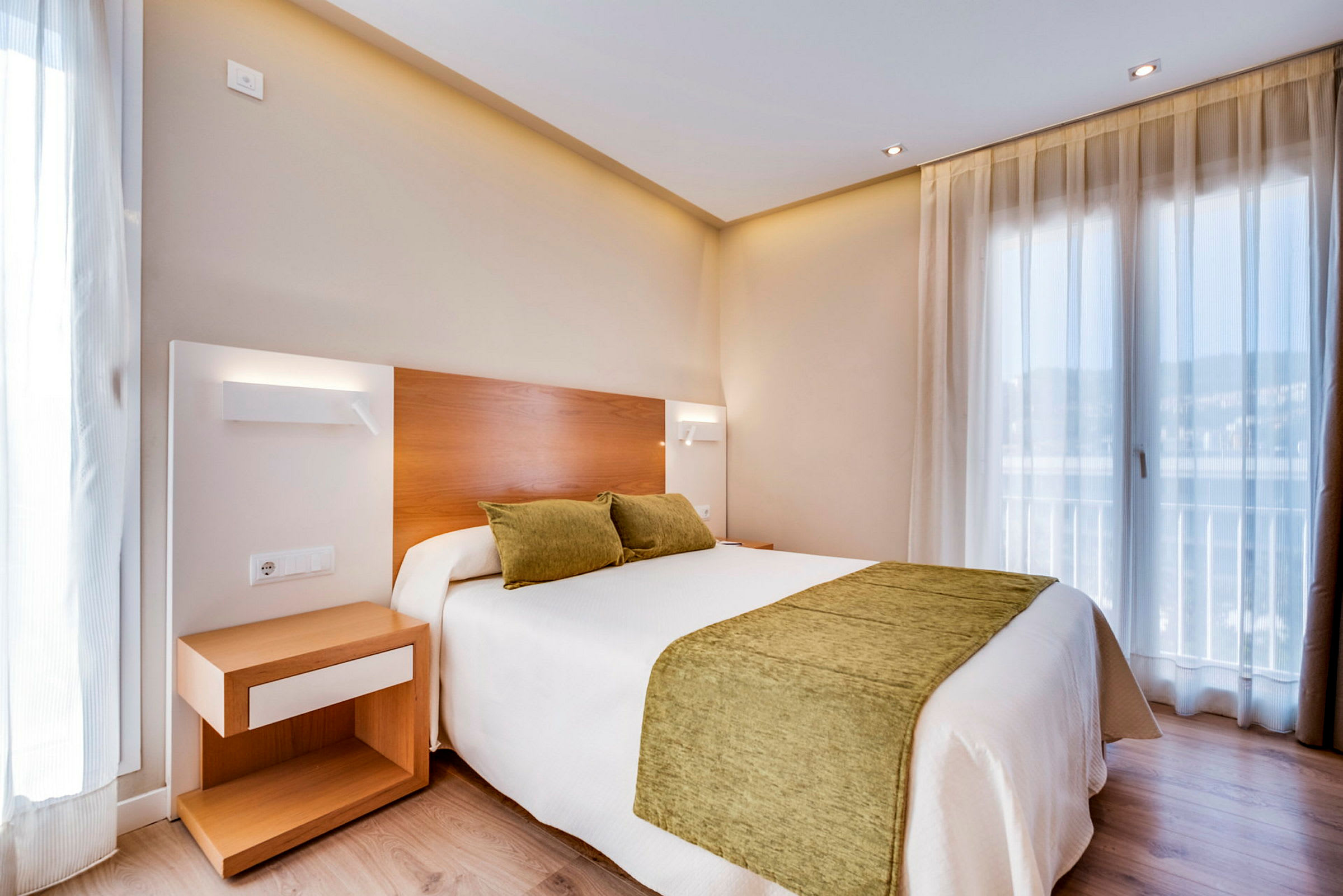 Ett hotellrum med en dubbelsäng med gröna kuddar och överkast. En nattduksbord står bredvid sängen. (AI-genererad text)