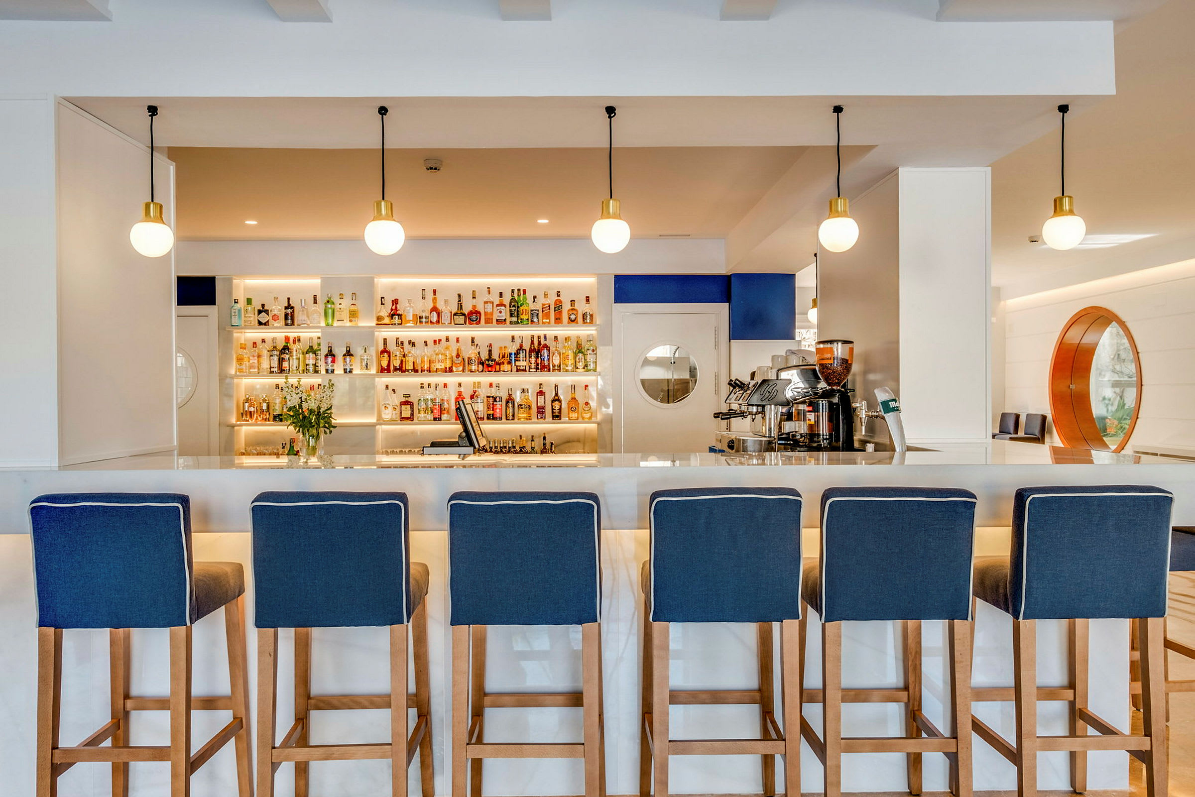 En bar med blåa barstolar framför en hylla med diverse drycker. (AI-genererad text)