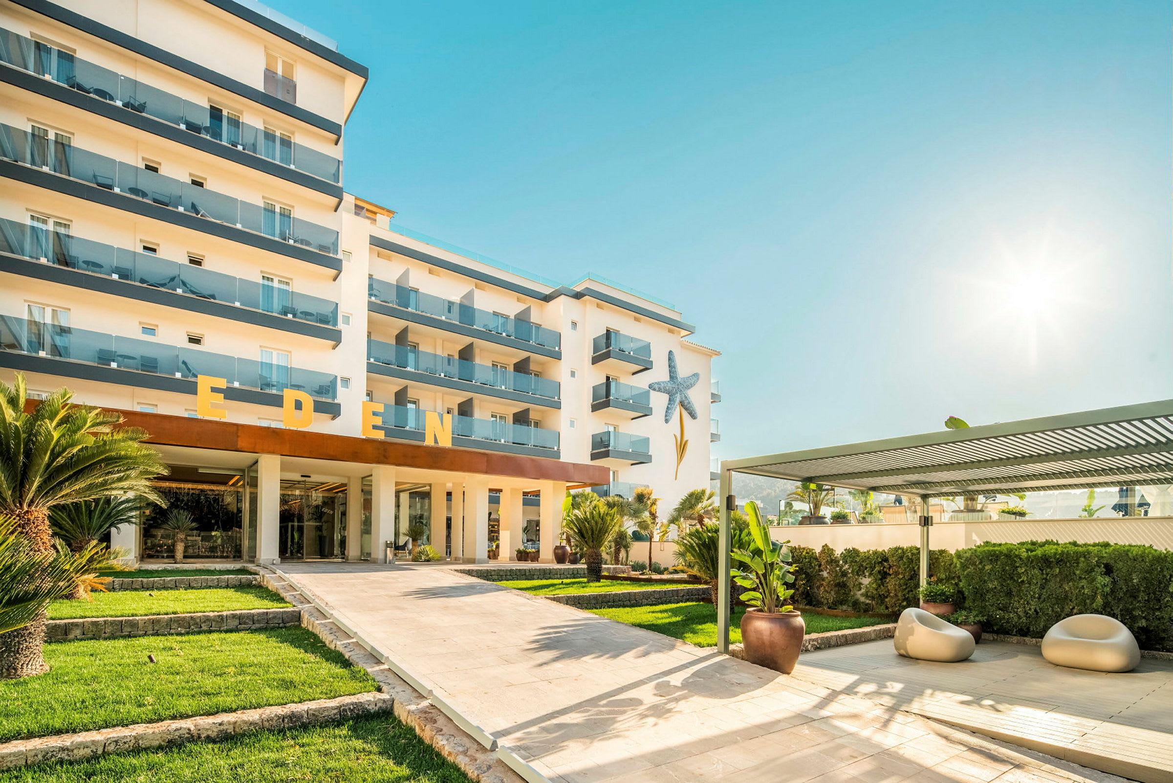 Bild av ett hotell med texten 'Eden' synlig på byggnaden, omgiven av grönska. (AI-genererad text)
