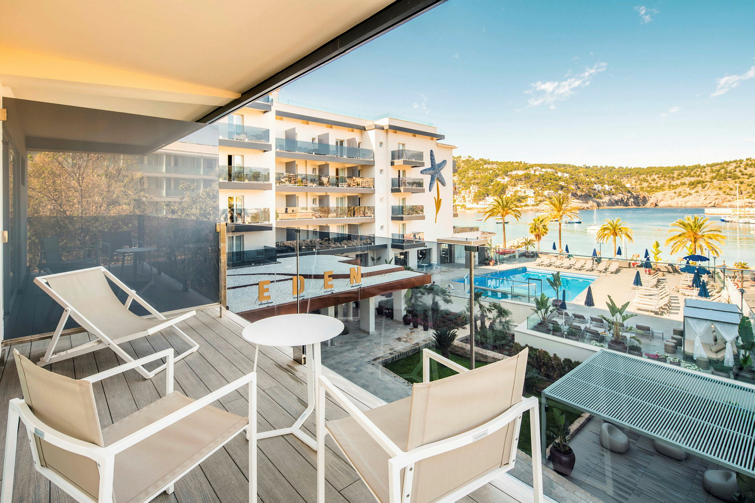 Vy från en terrass med sittplatser, utsikt över hotellområde med pool och hav. (AI-genererad text)