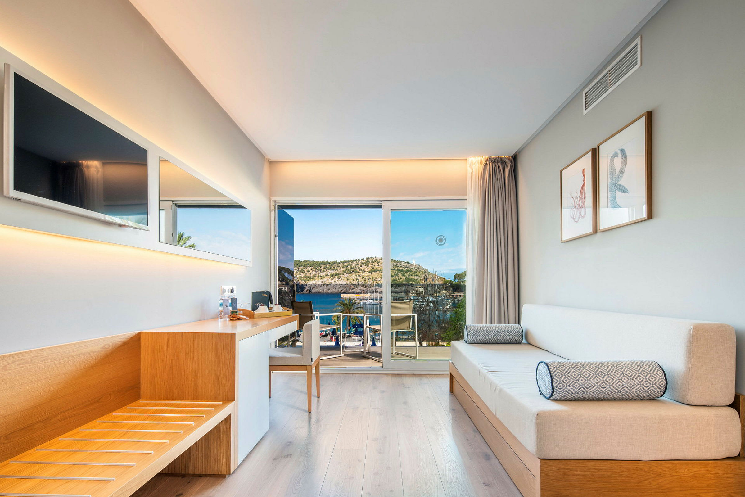 Ett modernt hotellrum med träinredning, soffa och utsikt över havet genom en glasdörr. (AI-genererad text)
