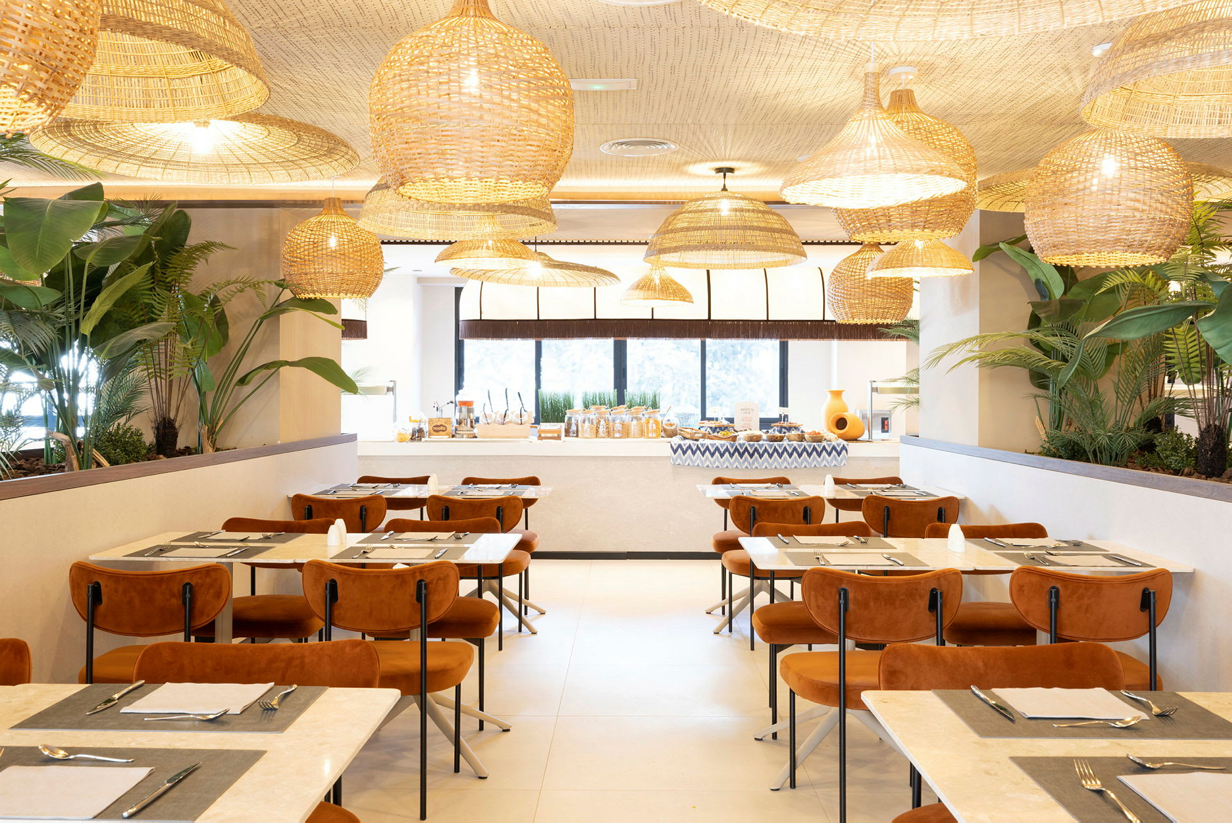 En elegant restaurang med moderna möbler, stora fönster, växter och hängande korglampor i taket. (AI-genererad text)