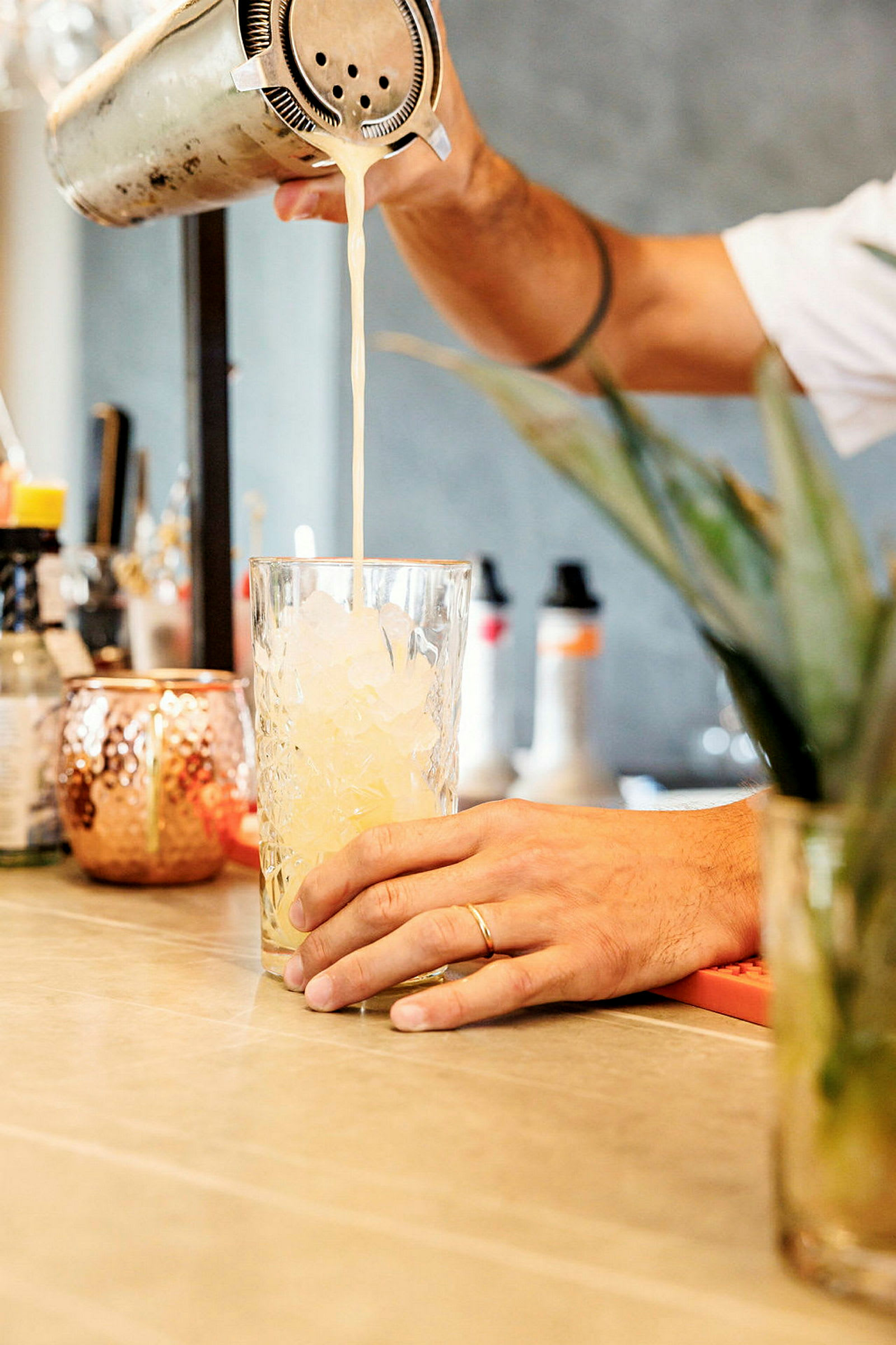 En person häller en drink från en shaker ner i ett glas fyllt med is. (AI-genererad text)