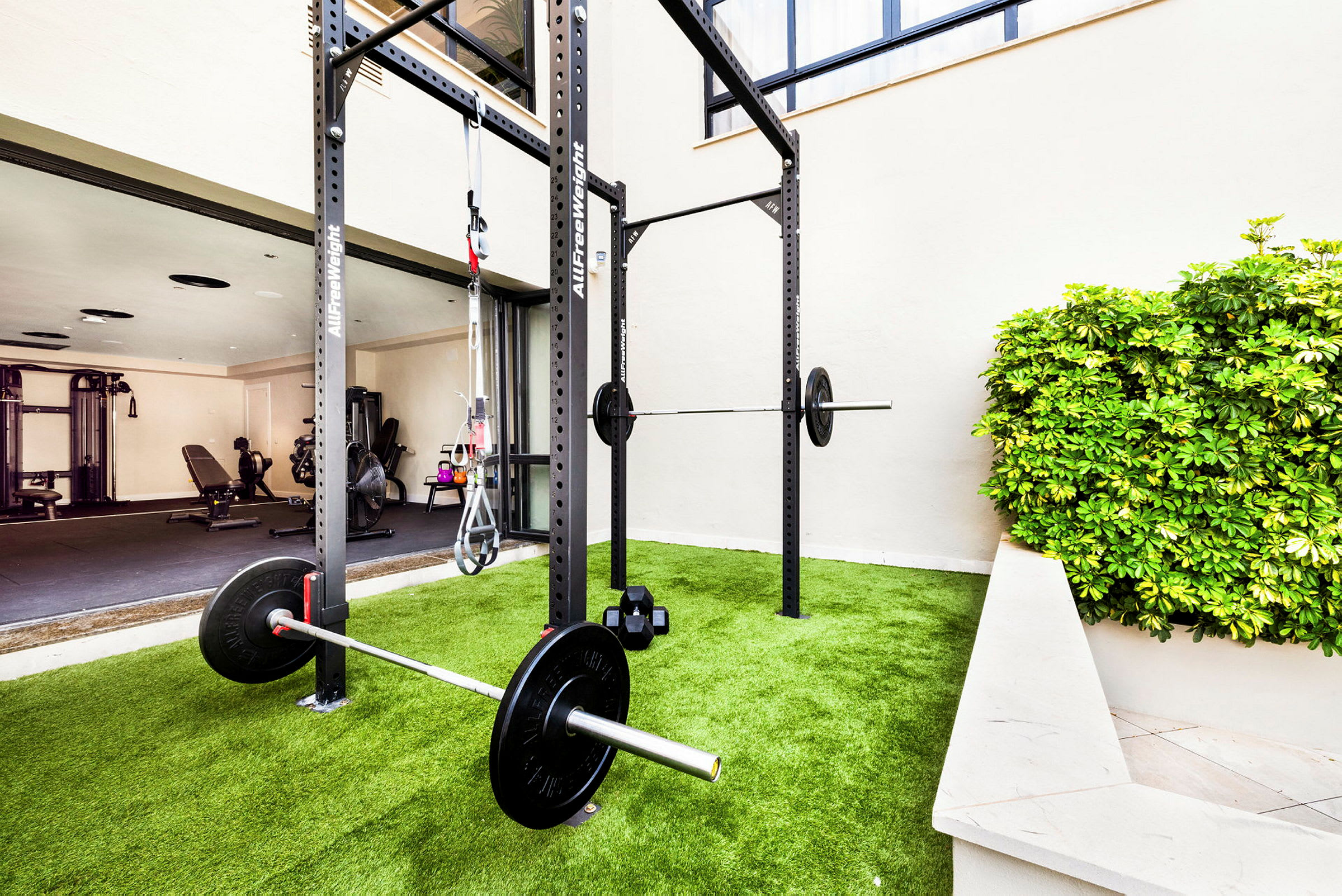 Bild på ett utomhusgym med träningsutrustning, inklusive tyngdlyftningsställ, på en gräsmatta. (AI-genererad text)