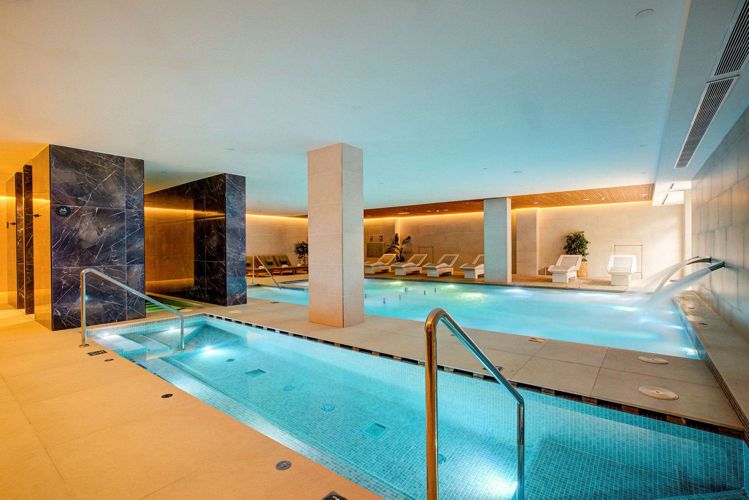 Ett modernt spa med en inomhuspool och avkopplingsområden. (AI-genererad text)