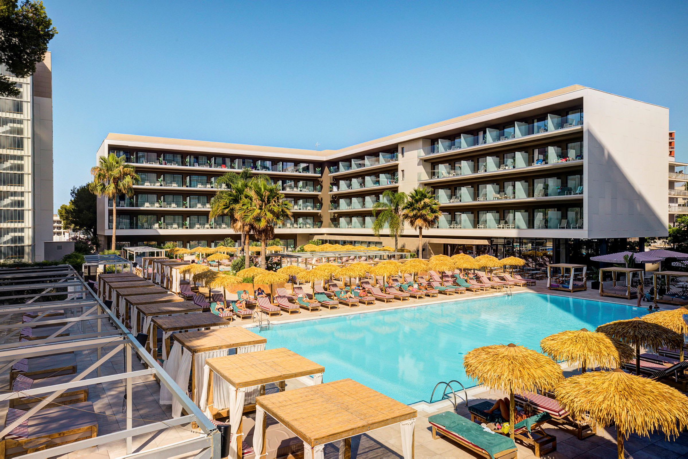 Ett modernt hotell med en stor pool, solstolar och parasoller, omgett av balkonger. (AI-genererad text)