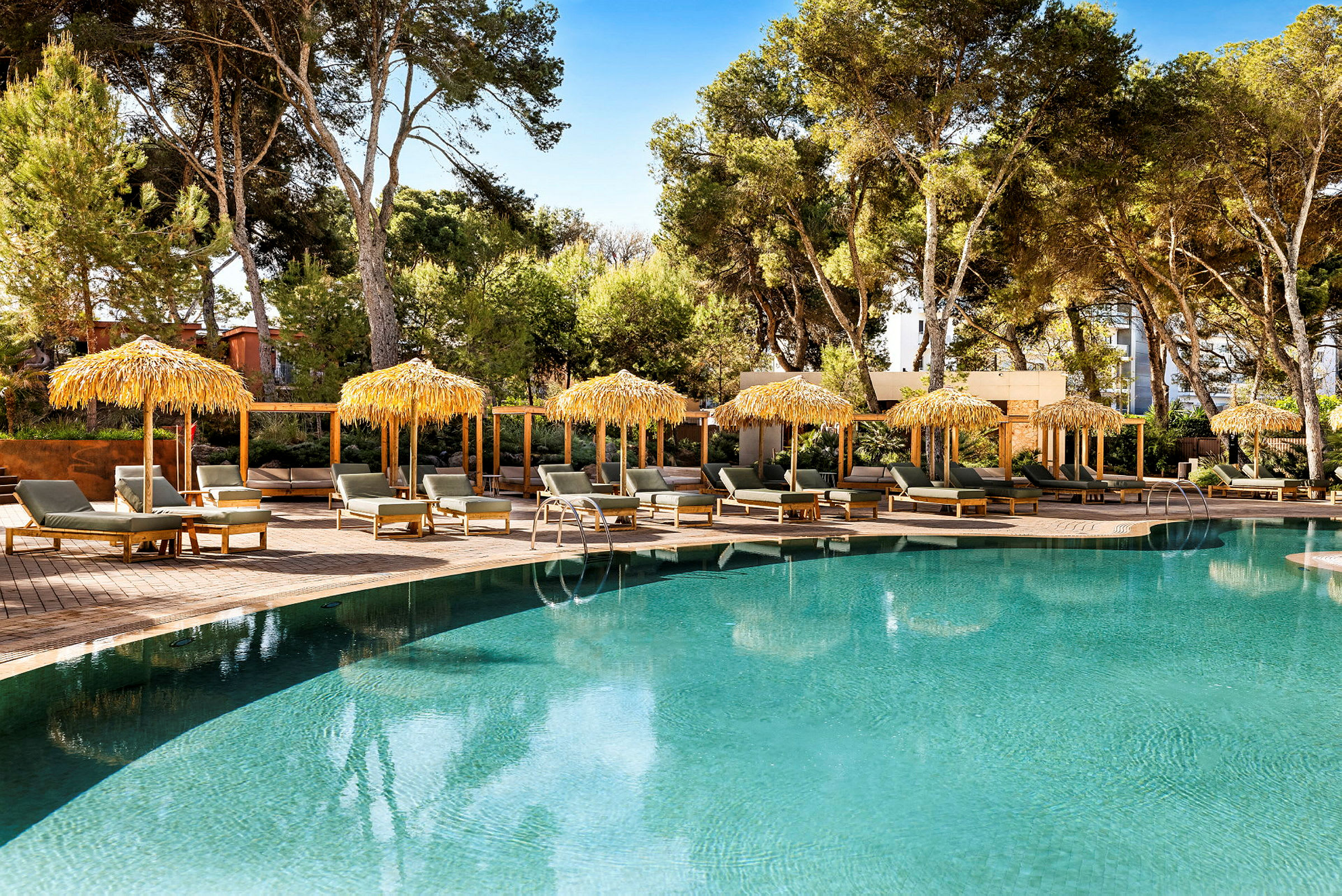 Poolområde med solstolar och parasoller vid sidan av en klar pool, omgiven av gröna träd. (AI-genererad text)