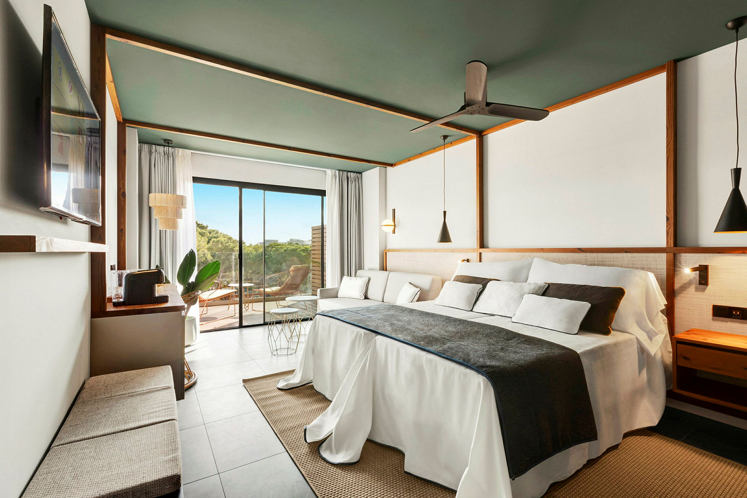 Ett modernt hotellrum med en stor bäddad säng, soffa och ett stort fönster mot en terrass. (AI-genererad text)