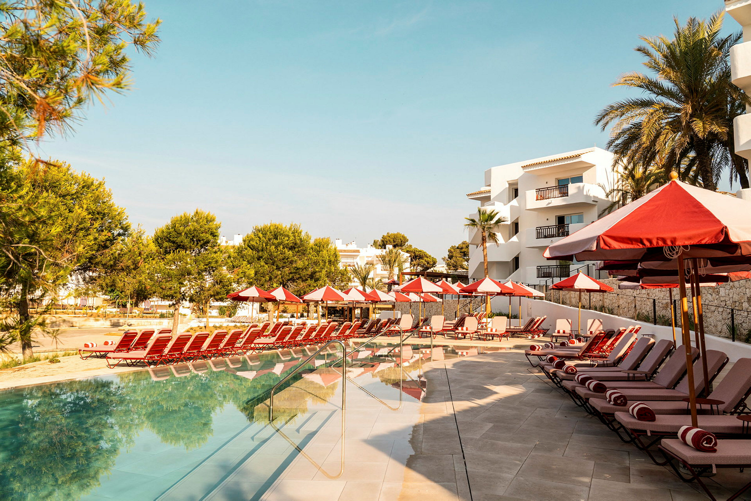 Bild av en hotellpool med solstolar och parasoller bredvid byggnader. (AI-genererad text)