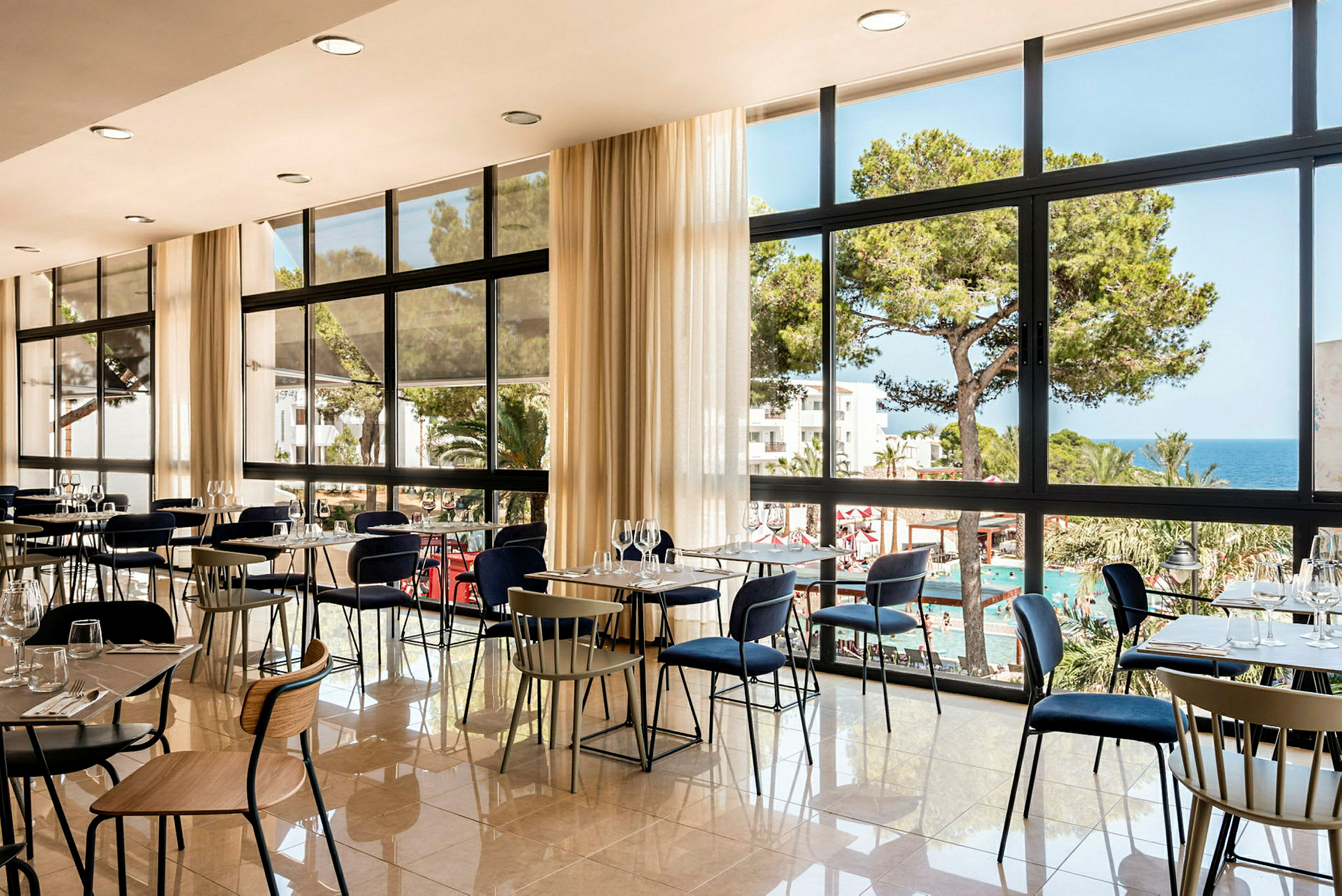En restaurang med stora fönster som vetter mot en pool och havsutsikt. (AI-genererad text)