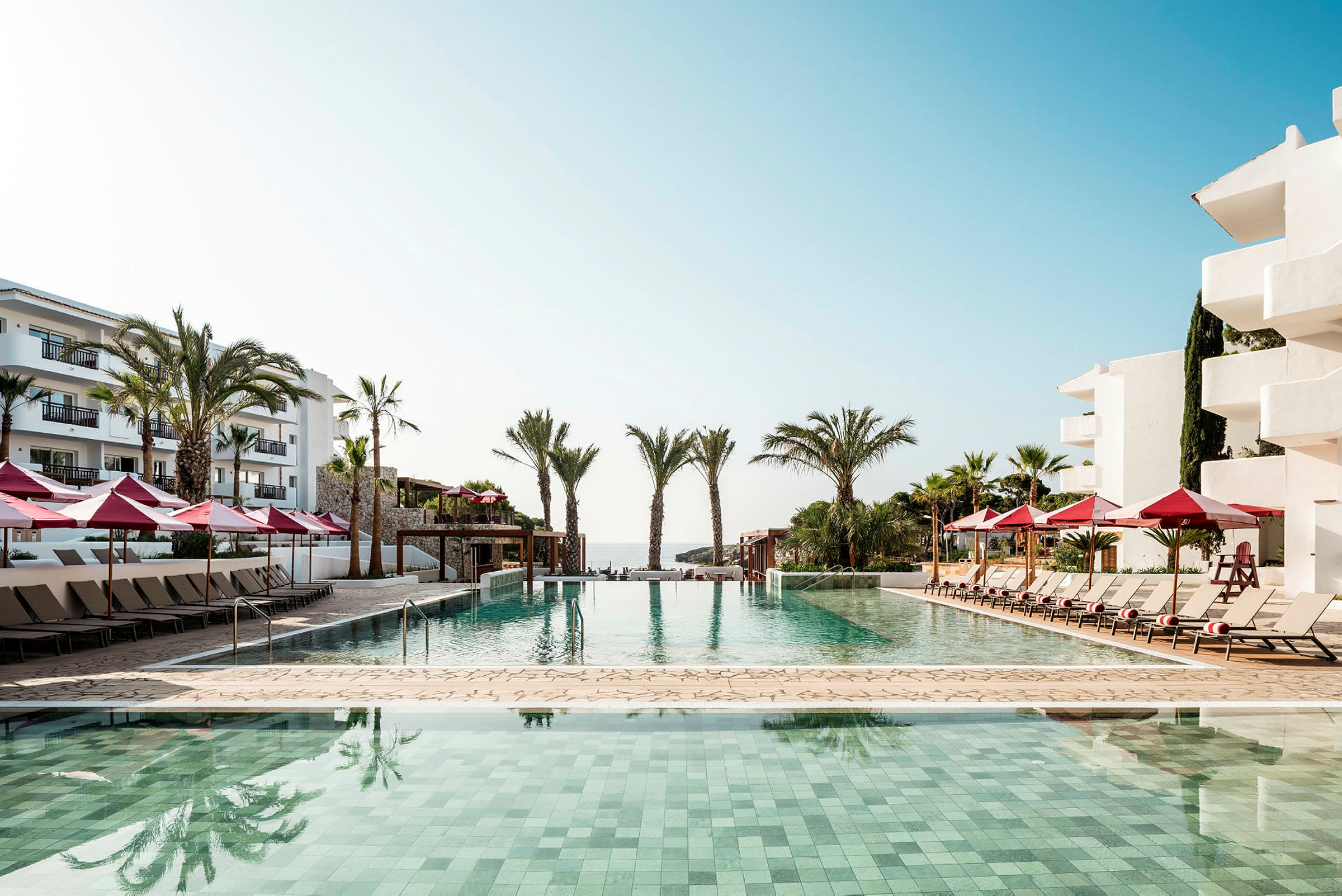 Utomhuspool vid kustnära hotell med solstolar och röda parasoller. (AI-genererad text)