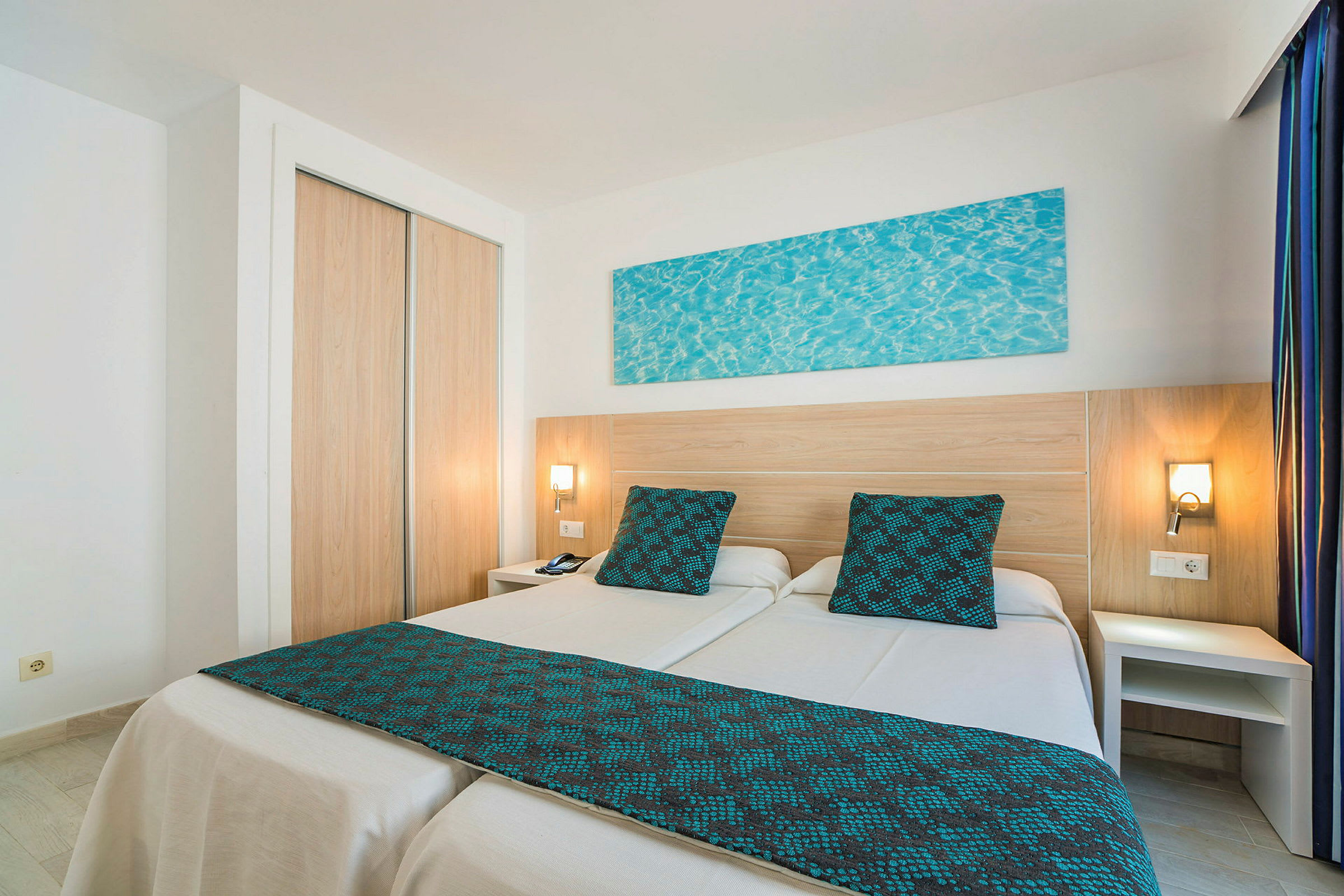 Ett hotellrum med två enkelsängar med blå detaljer. (AI-genererad text)
