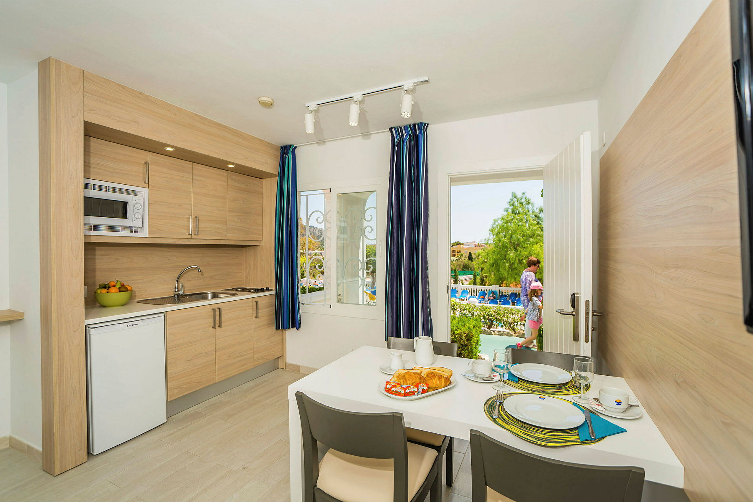 En hotelllägenhet med ett kök och en matplats som vetter mot en terrass och poolområdet. (AI-genererad text)