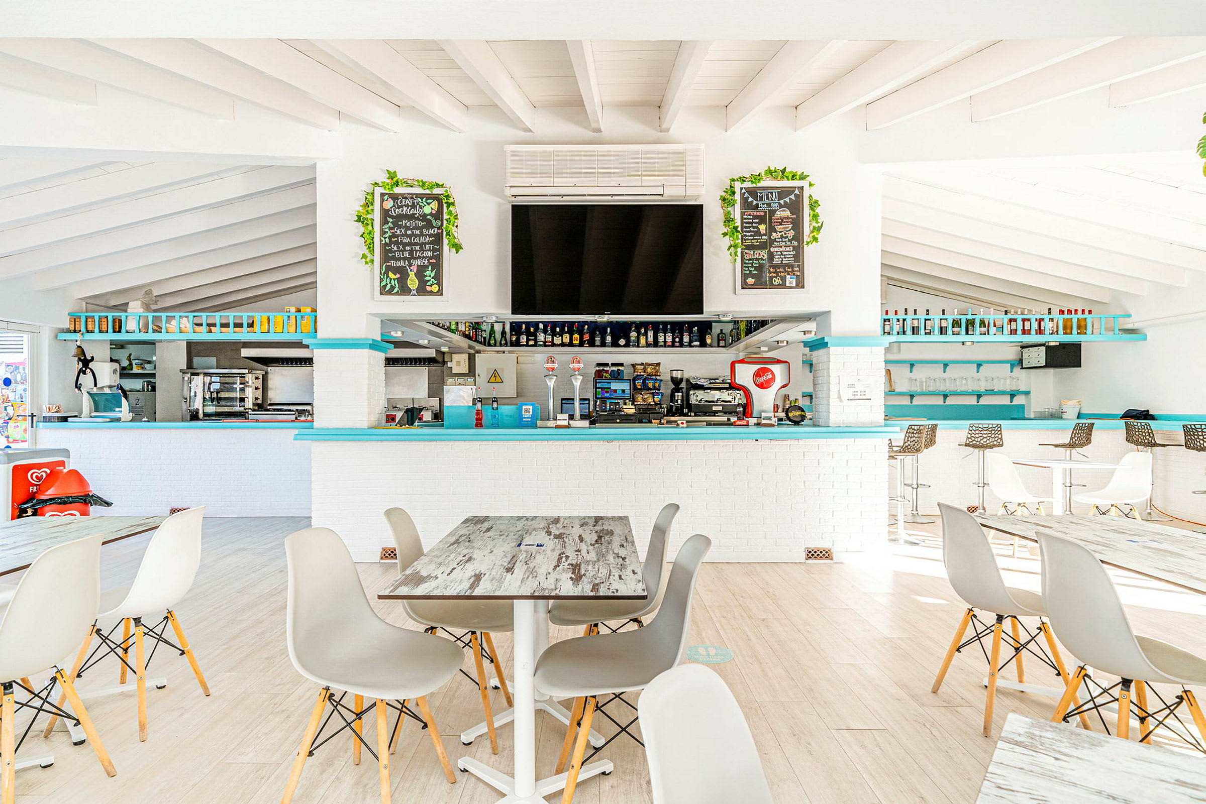 Interiör av en ljus restaurang med sittplatser och en bar. (AI-genererad text)