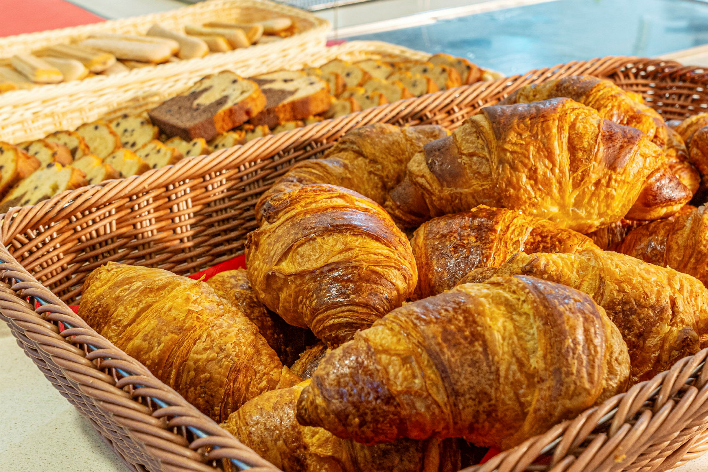 En korg med croissanter framför en bakgrund med olika bakverk. (AI-genererad text)