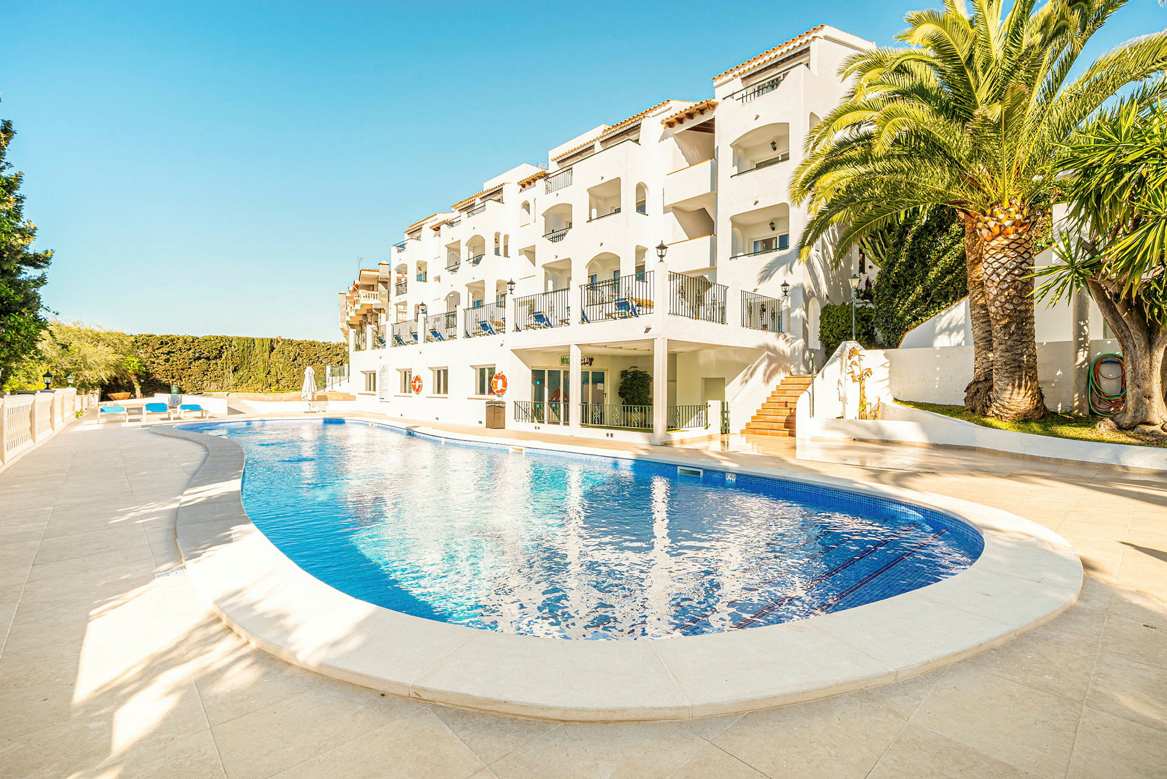 Bild av ett hotell med en pool framför byggnaden, omgiven av palmer och grönska. (AI-genererad text)