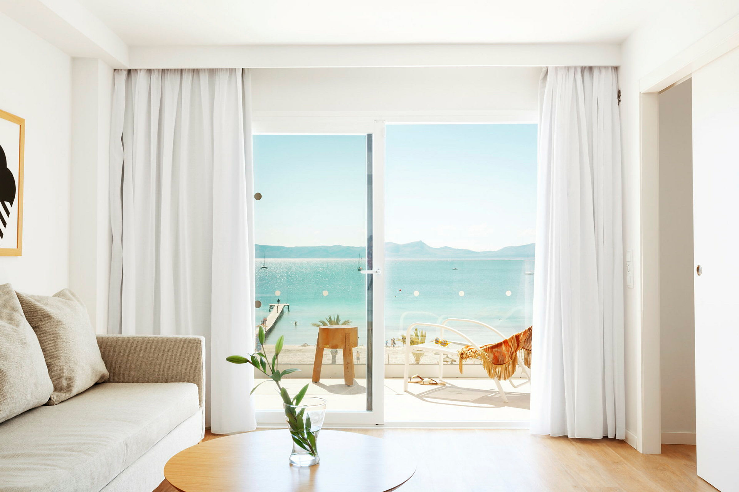 Bild av ett ljust rum med en soffa, ett bord och glasdörrar som leder till en balkong med utsikt över havet. (AI-genererad text)