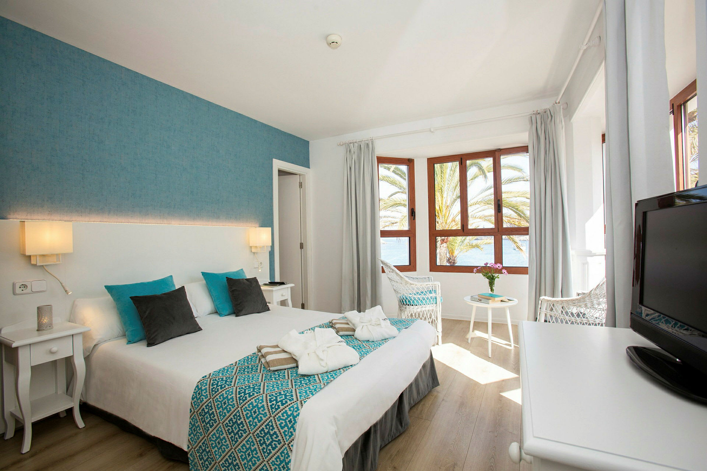 Hotellrum med dubbelsäng, fönster och utsikt över havet. (AI-genererad text)