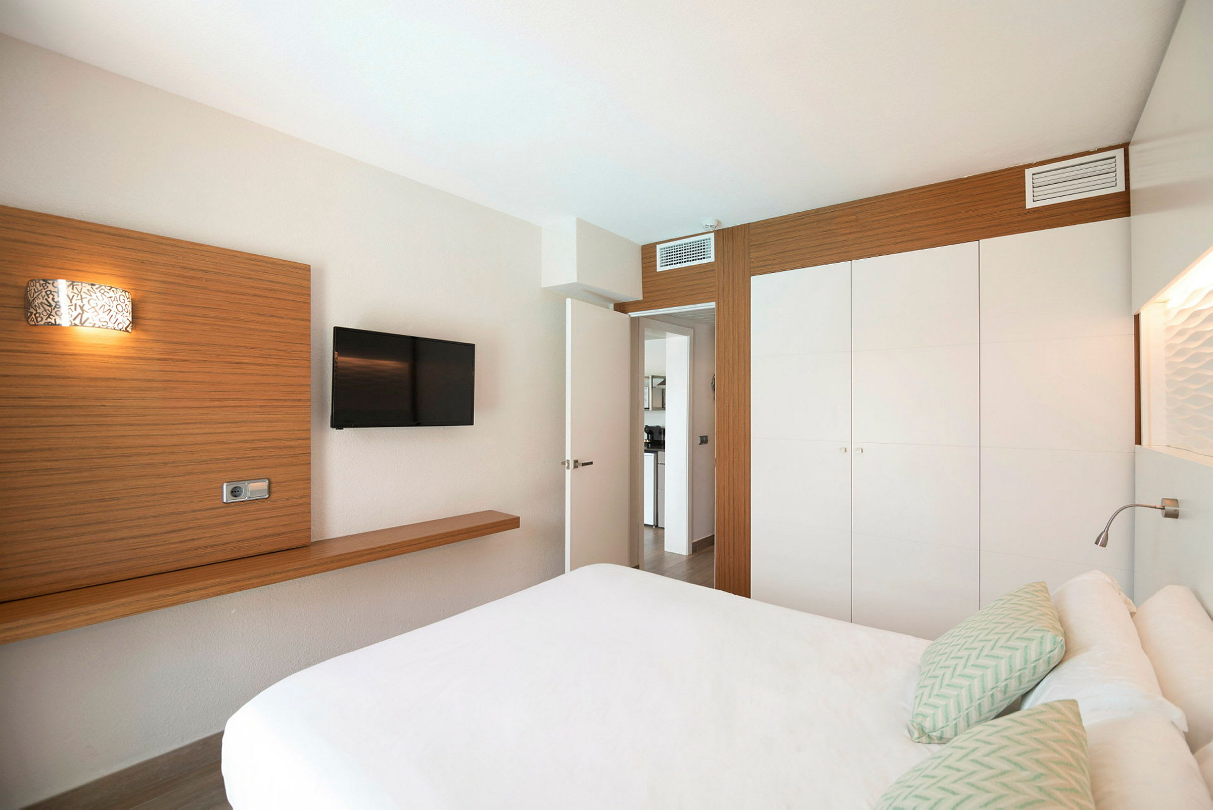 En hotellrum med inredning som inkluderar en säng, en väggmonterad TV och en vit garderob. (AI-genererad text)