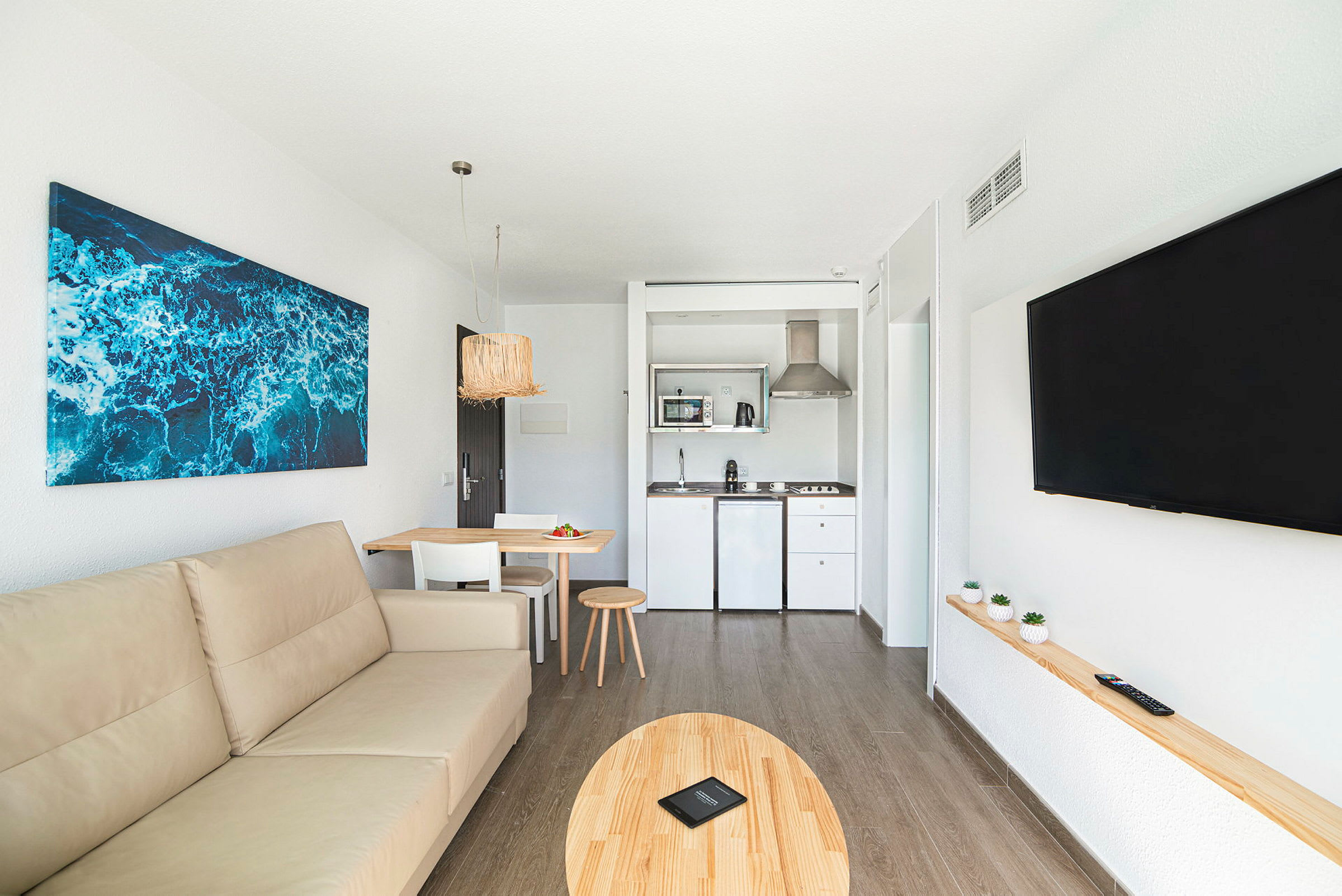 Ett vardagsrum med en beige soffa, ett matbord och ett kök i bakgrunden. (AI-genererad text)