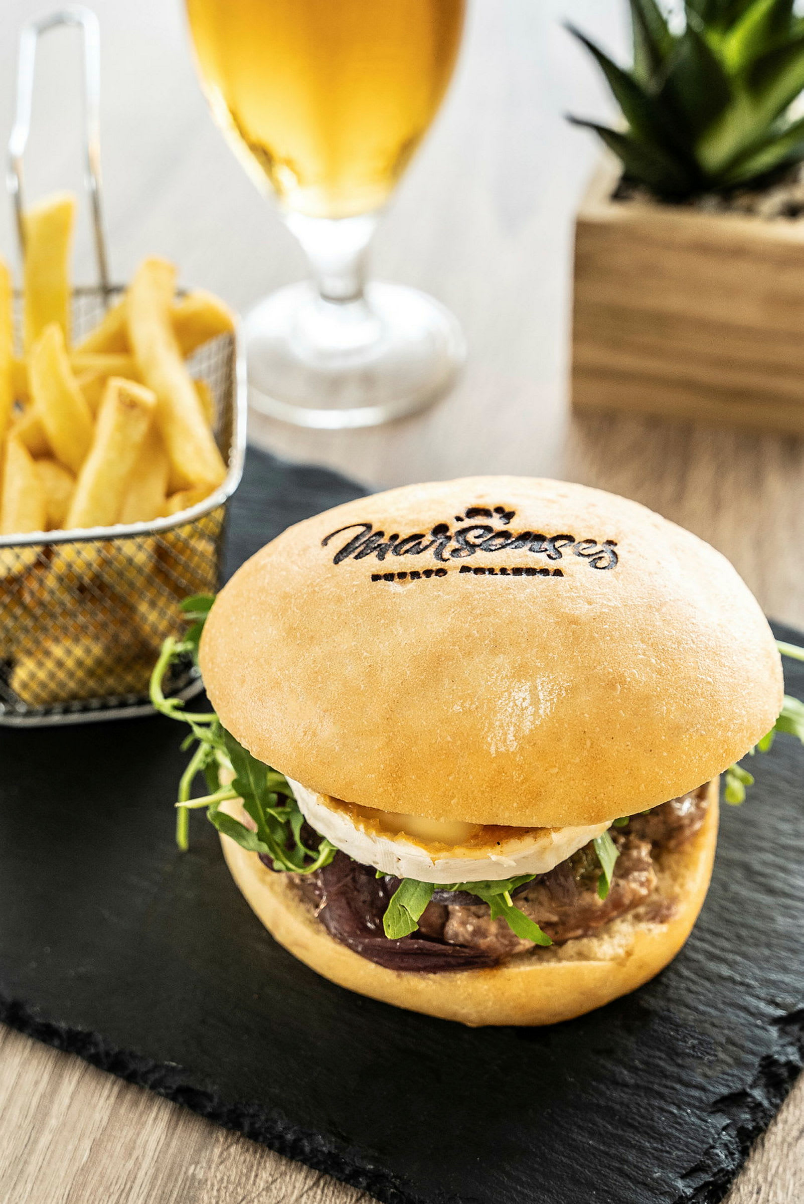 Närbild på en hamburgare serverad med pommes frites och ett glas öl i bakgrunden. (AI-genererad text)