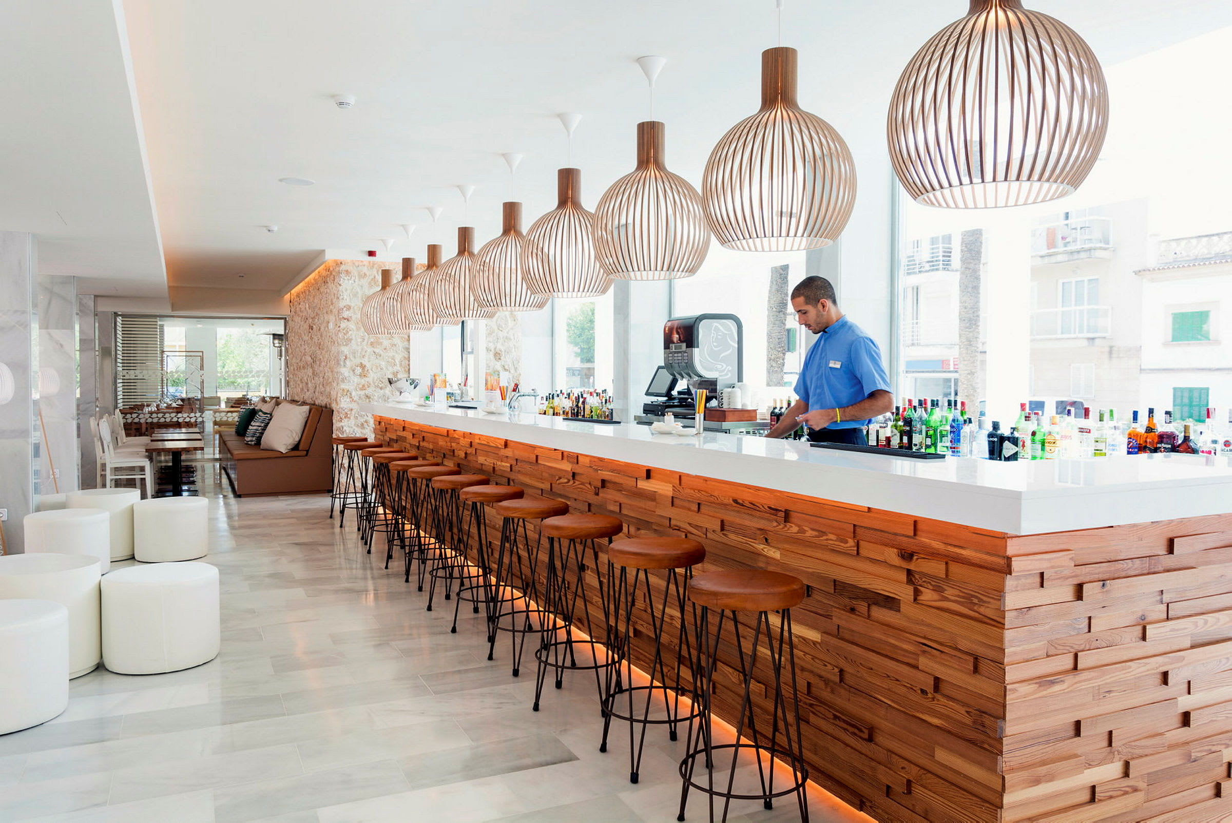 En modern bar med trädetaljer och stora lampor hänger ovanför bardisken. (AI-genererad text)