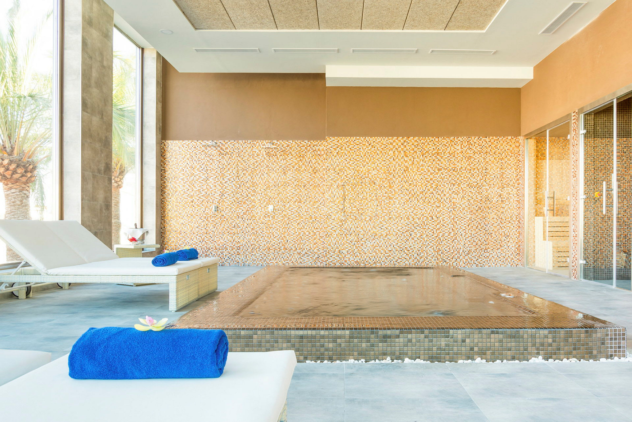 Interiör av ett spa med vilstolar och en pool omgiven av mosaikväggar. (AI-genererad text)