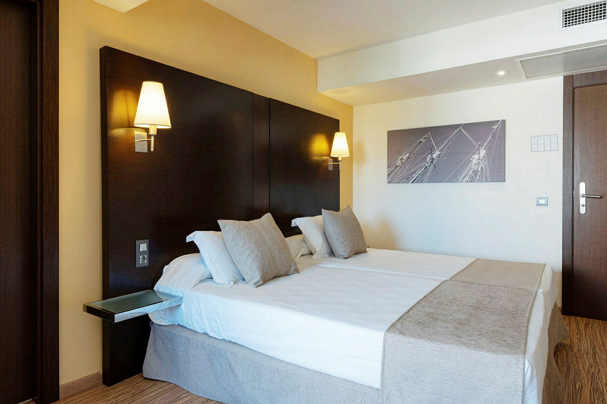 Ett hotellrum med en dubbelsäng, väggmonterade lampor och en modern inredning. (AI-genererad text)
