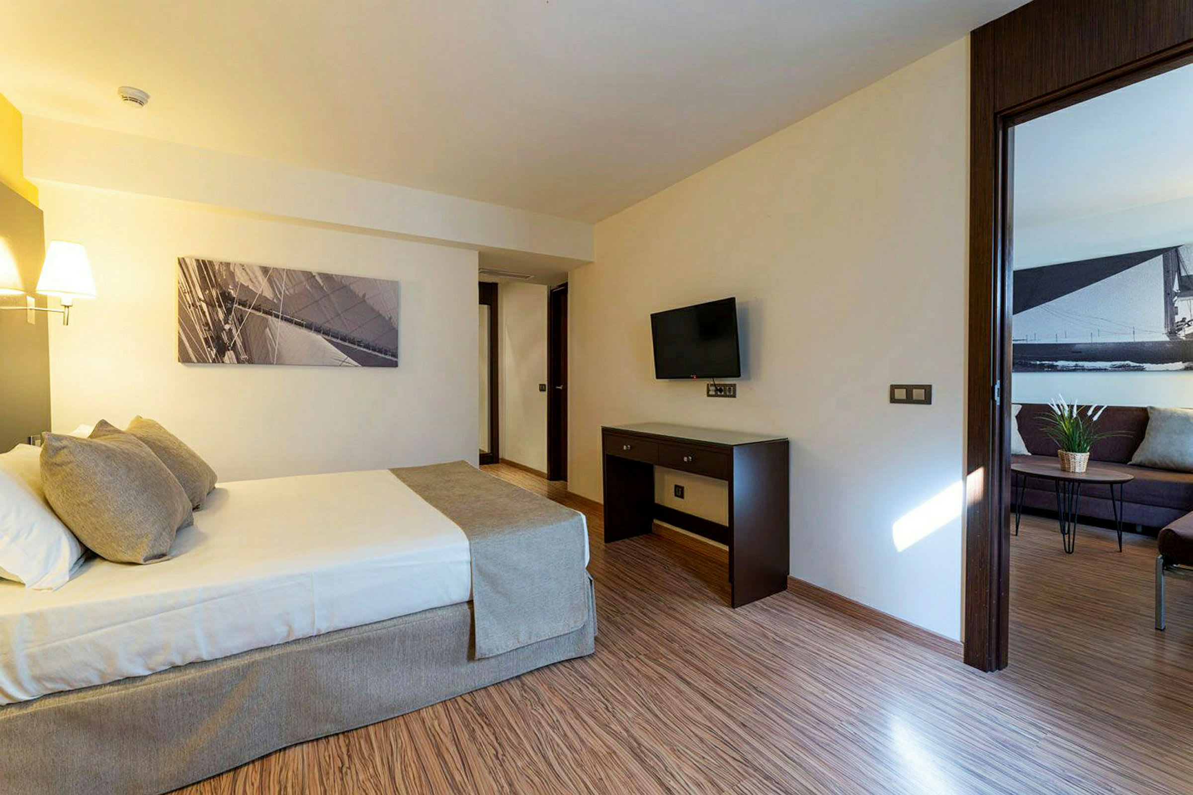 Ett hotellrum med en säng, en TV på väggen och ett bord. Dörren leder till ett vardagsrum. (AI-genererad text)