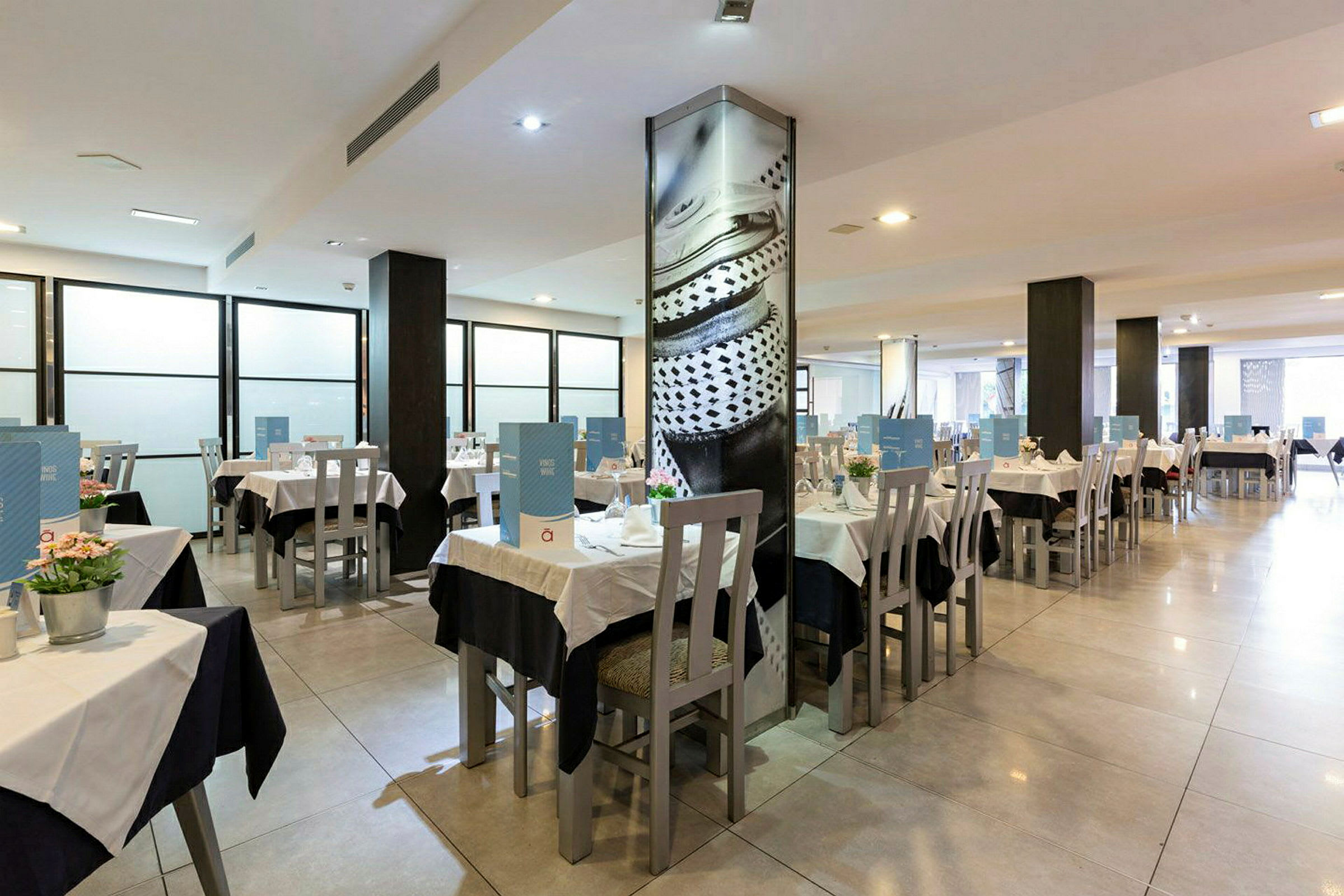 Bild av en restaurang med dukade bord och stolar i en ljus och rymlig miljö. (AI-genererad text)