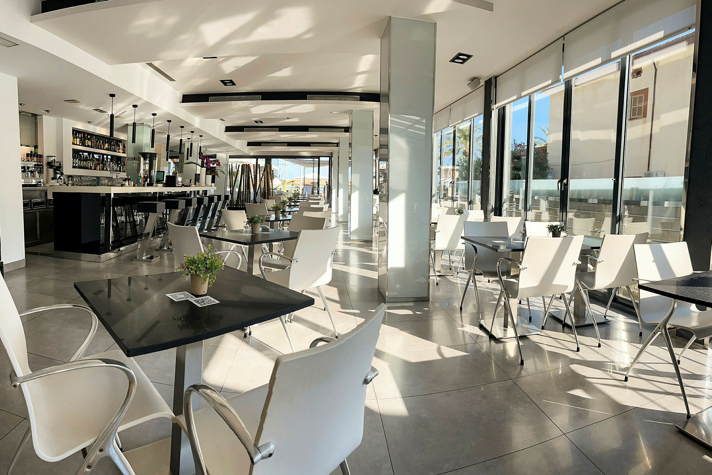 En modern restaurang med vita stolar och bord, samt en lång bar till vänster. (AI-genererad text)