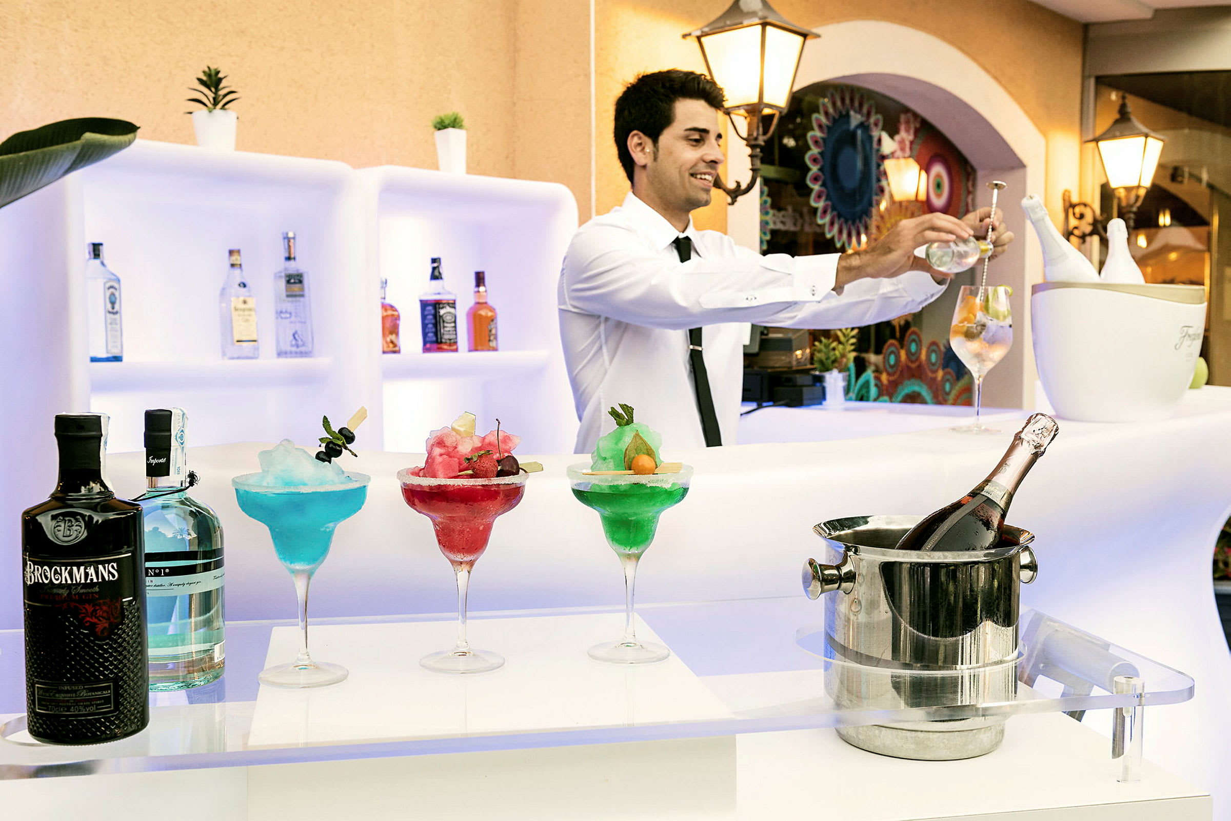 En bardisk med färgglada cocktails, flaskor och en ishink med en flaska champagne. (AI-genererad text)