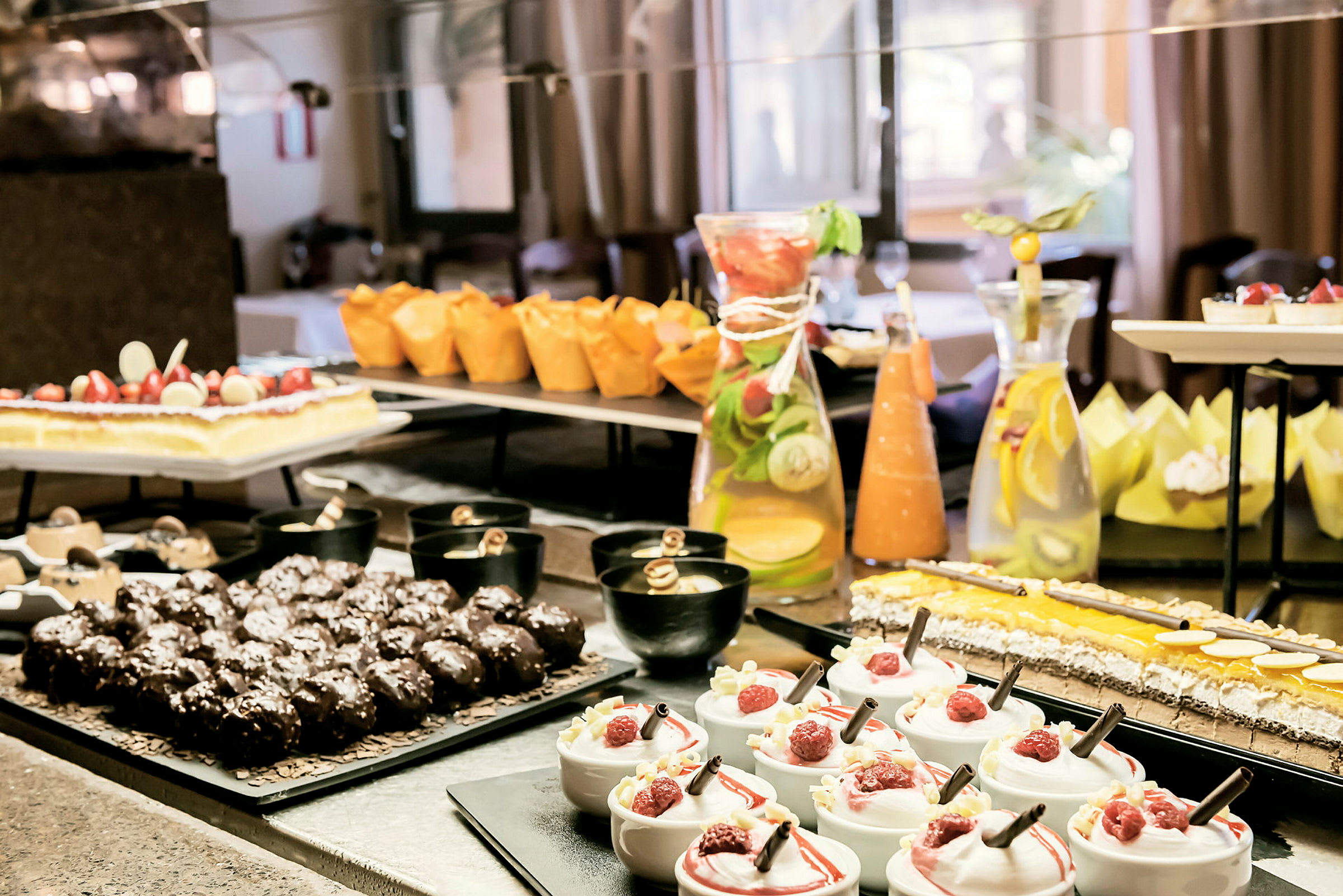 Ett dessertbord med olika sorters bakverk, mousse med hallon, chokladmuffins och en karaff med citronvatten. (AI-genererad text)