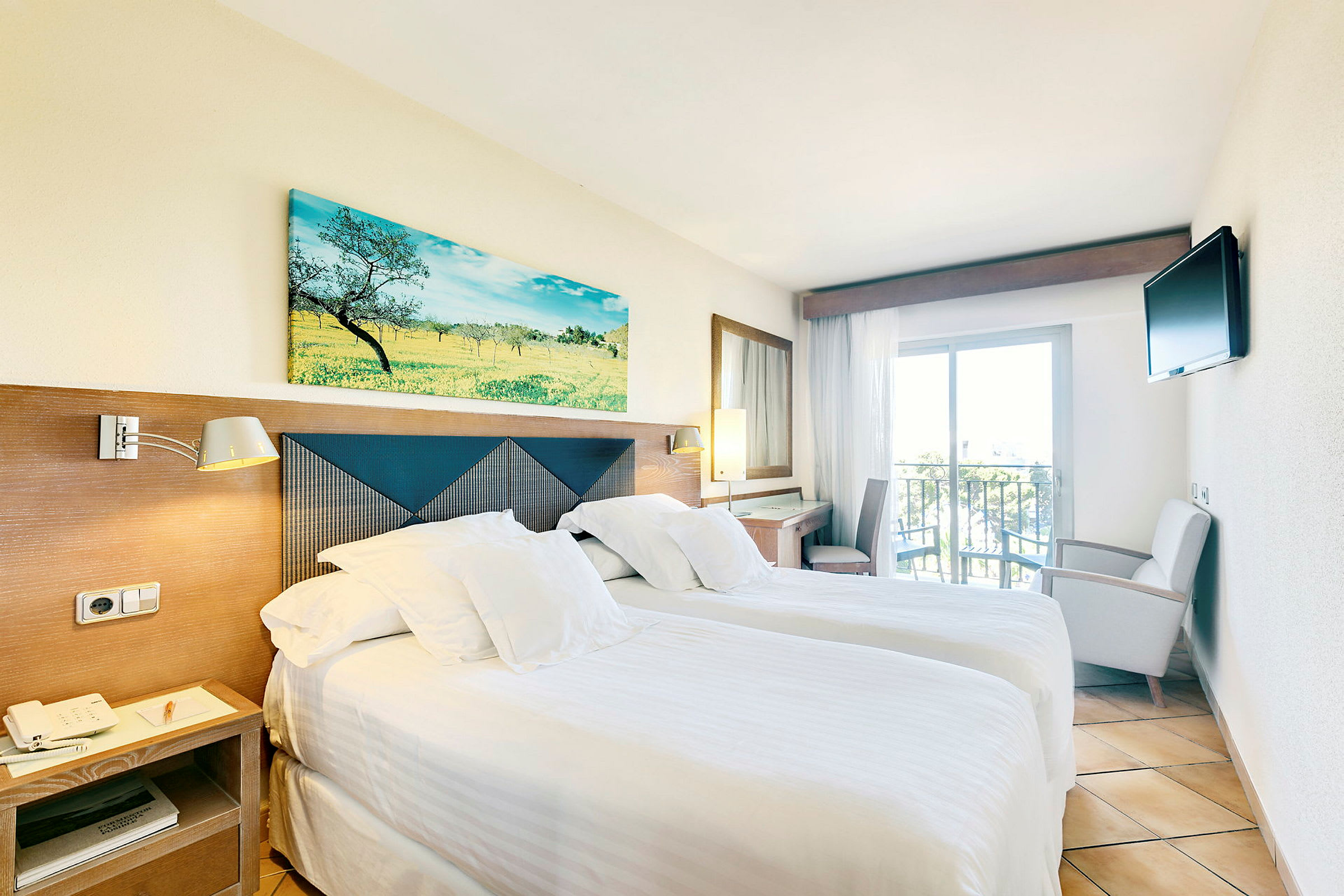 Ett hotellrum med två enkelsängar, ljusa sängkläder, en tavla ovanför huvudgaveln, en liten balkong och en TV på väggen. (AI-genererad text)