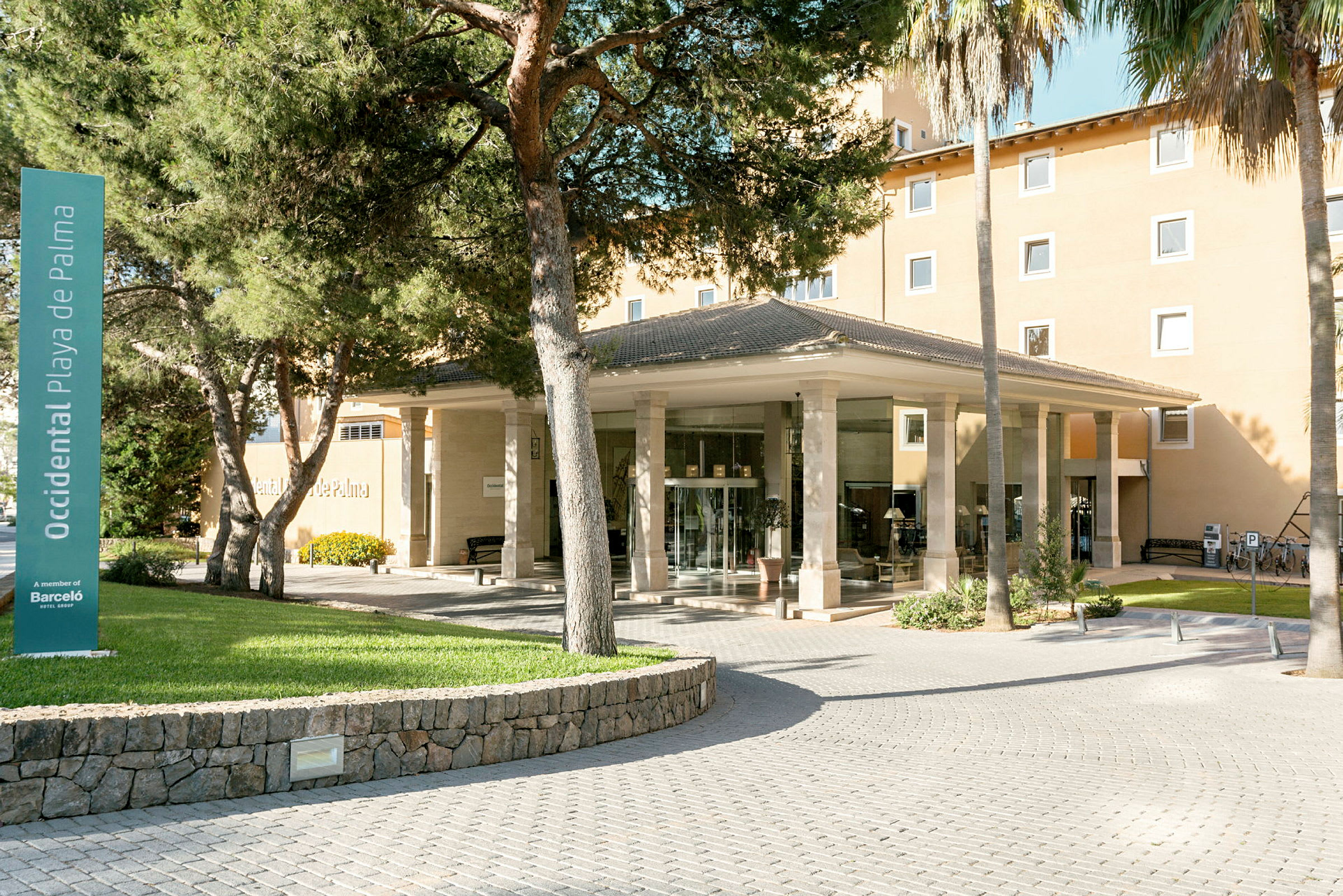 Entrén till ett hotell omgivet av träd och gröna ytor. (AI-genererad text)