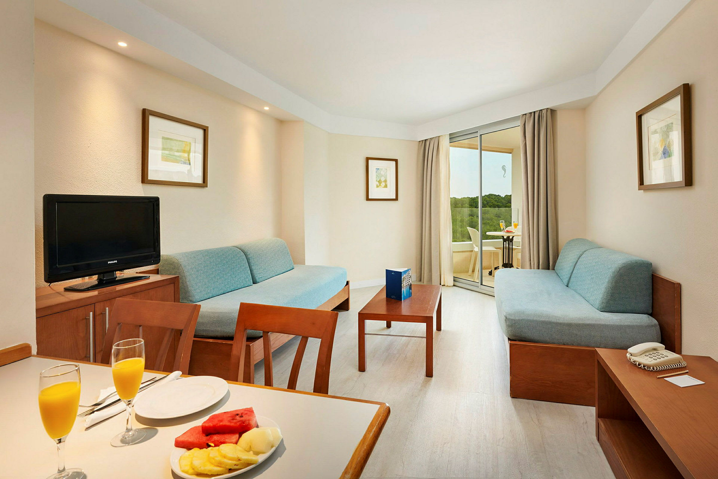 Ett hotellrum med två soffor, ett soffbord och en balkong i bakgrunden. (AI-genererad text)