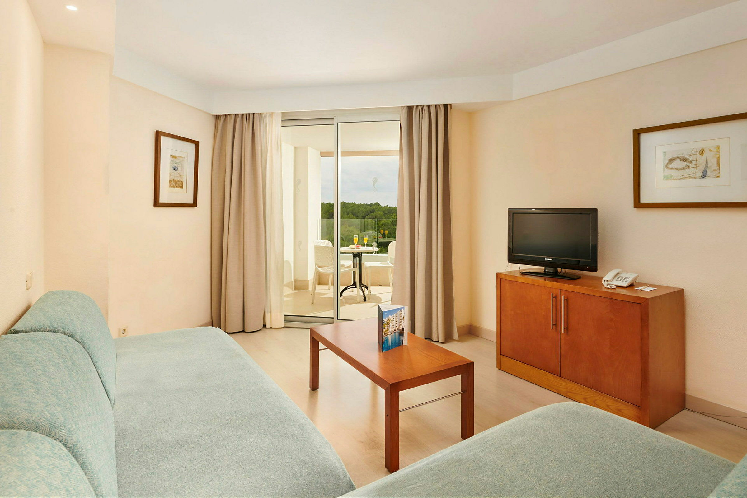 Hotellrum med sittgrupp, bord och TV, samt balkong med utsikt. (AI-genererad text)