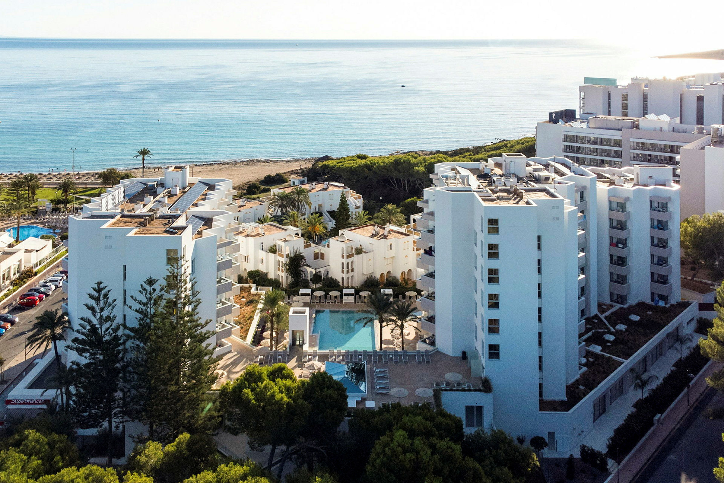 Utsikt över hotellbyggnader med pool, palmträd och hav i bakgrunden. (AI-genererad text)