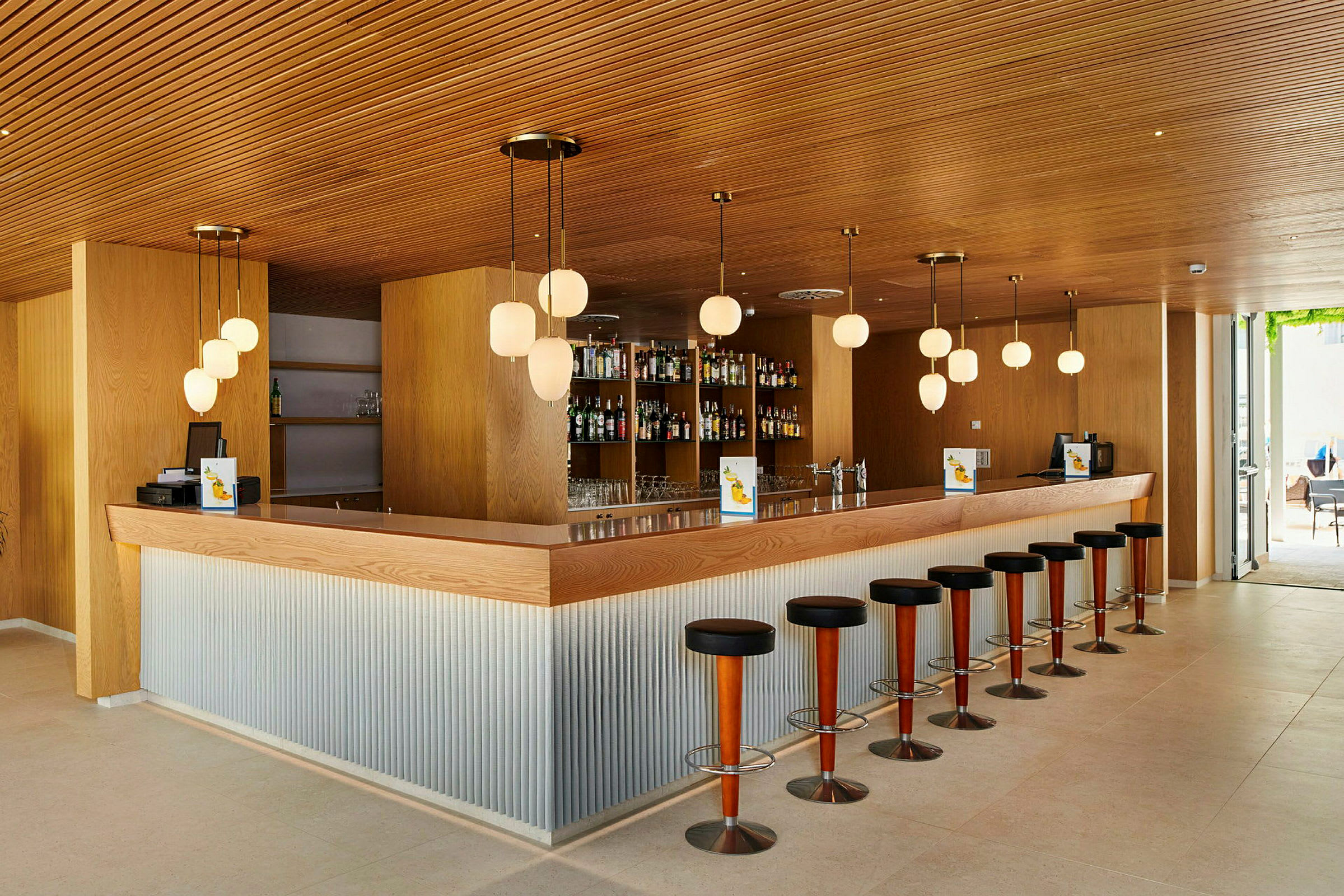 En stilren bar med träpaneler, bardisk och höga barstolar. (AI-genererad text)