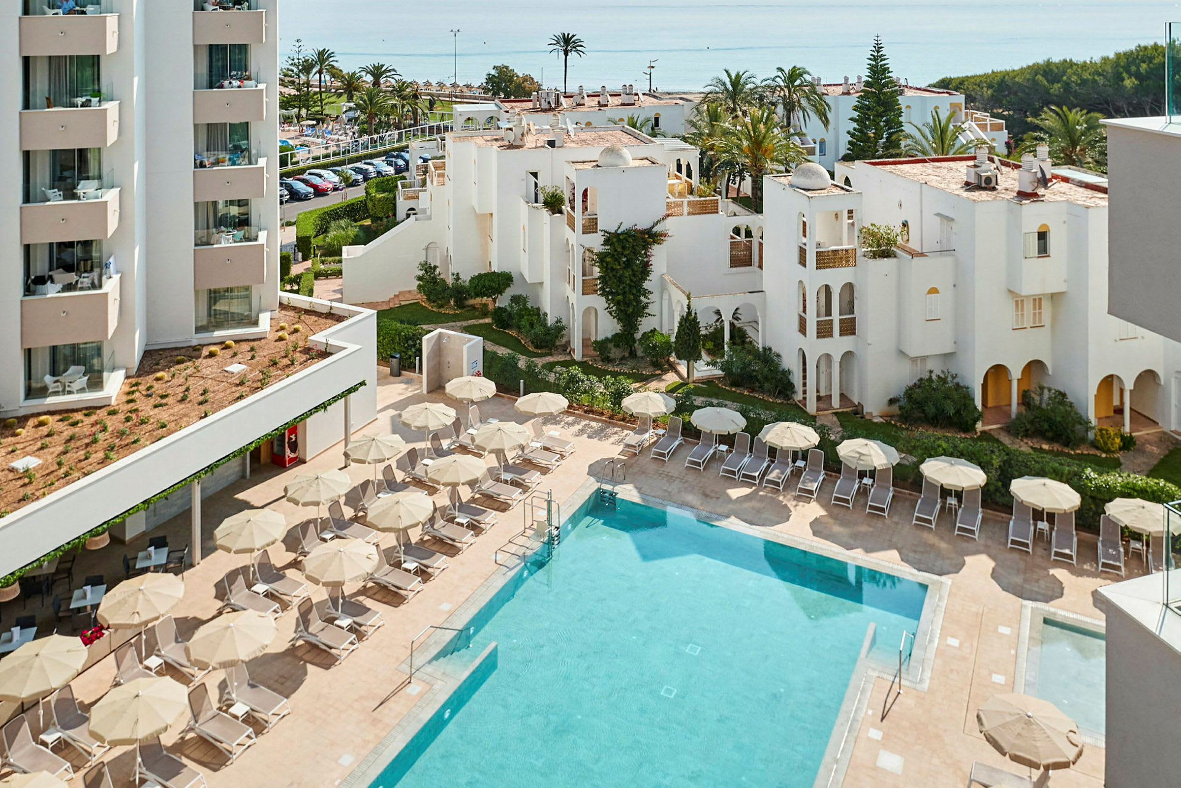 Hotellområde med pool, solstolar och parasoller samt vita byggnader i bakgrunden. (AI-genererad text)