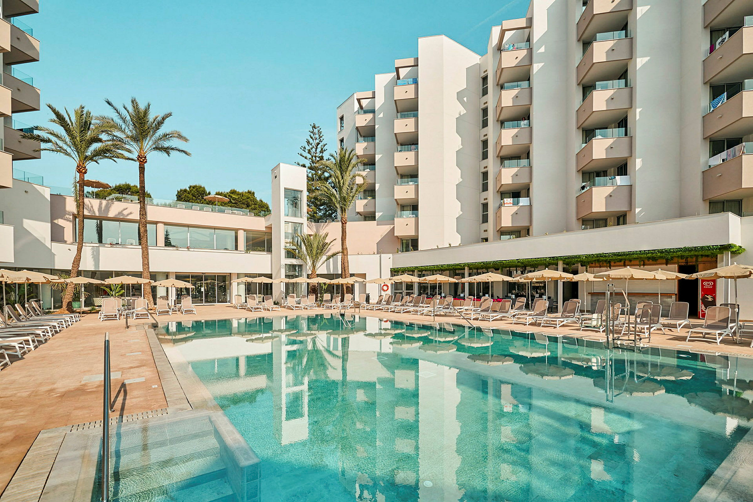 Ett hotell med balkonger omger en pool med solstolar och parasoller. (AI-genererad text)